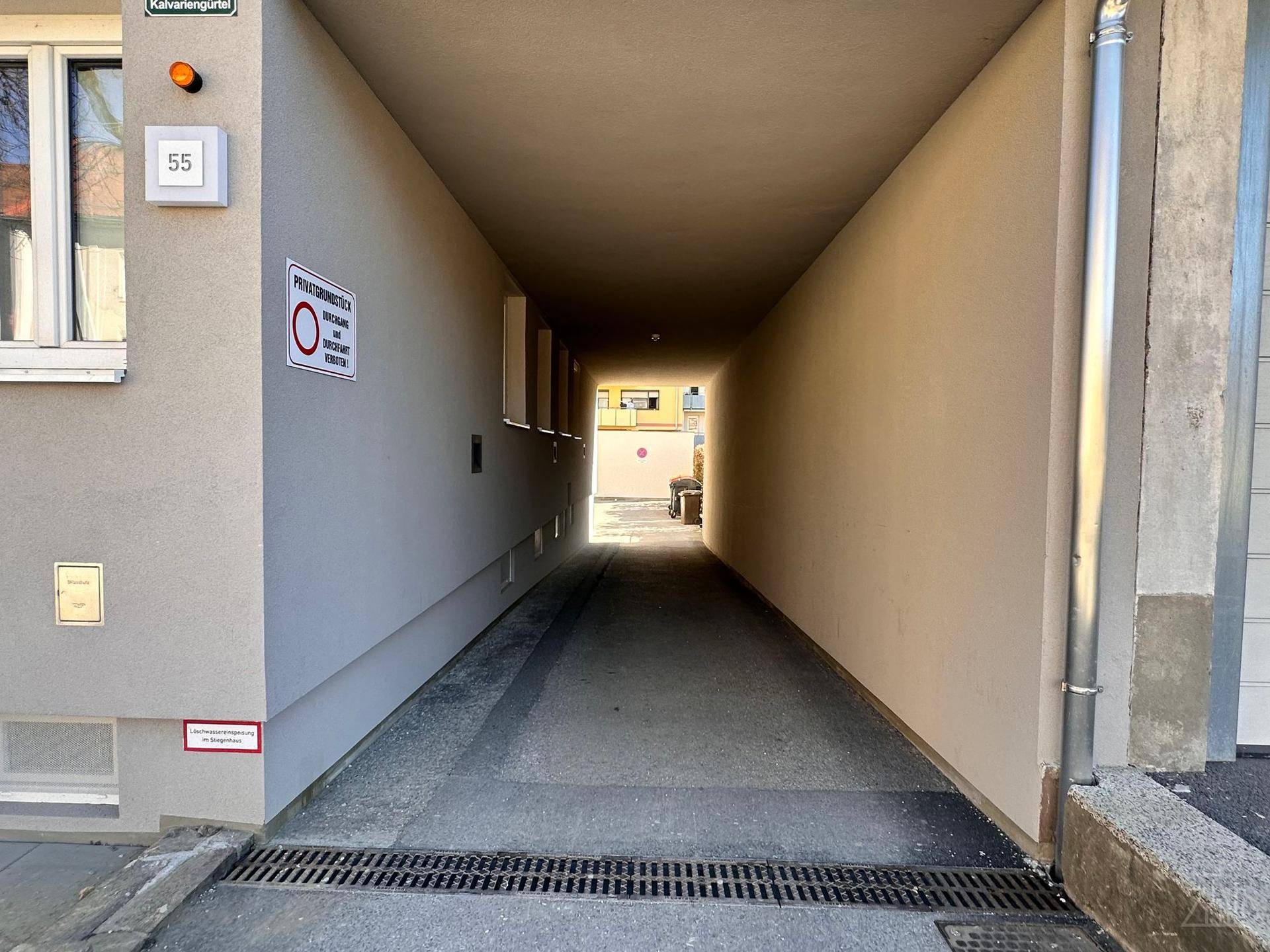 Überdachter Durchgang zum Innenhof eines Wohngebäudes mit Hinweisschildern.