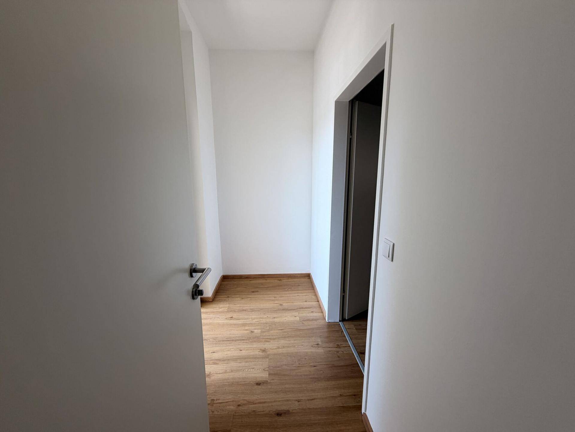 Heller Flur mit Laminatboden und weißen Wänden, der zu weiteren Räumen führt.