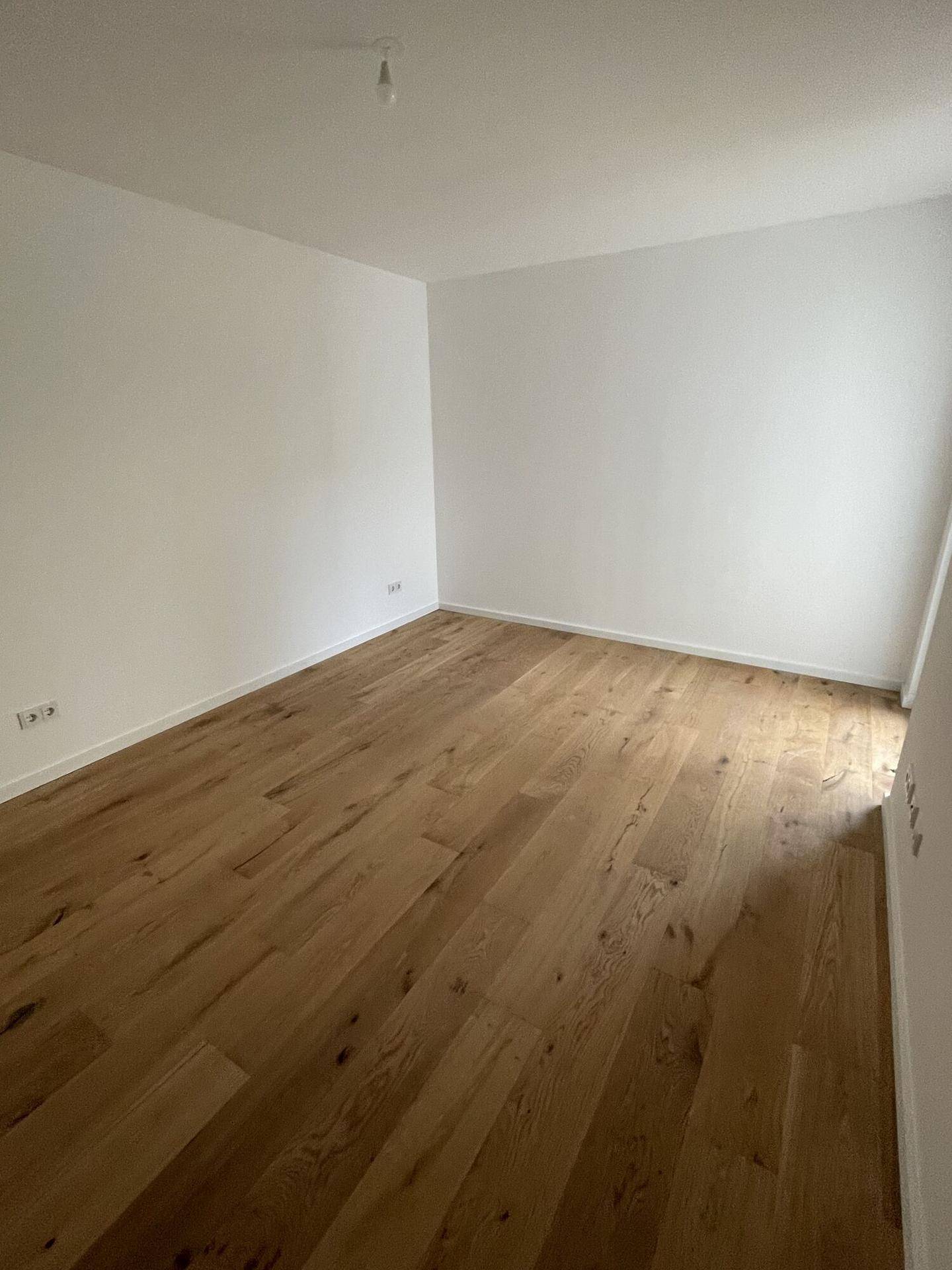 Heller, leerer Raum mit neuem Holzparkettboden und frisch gestrichenen weißen Wänden.