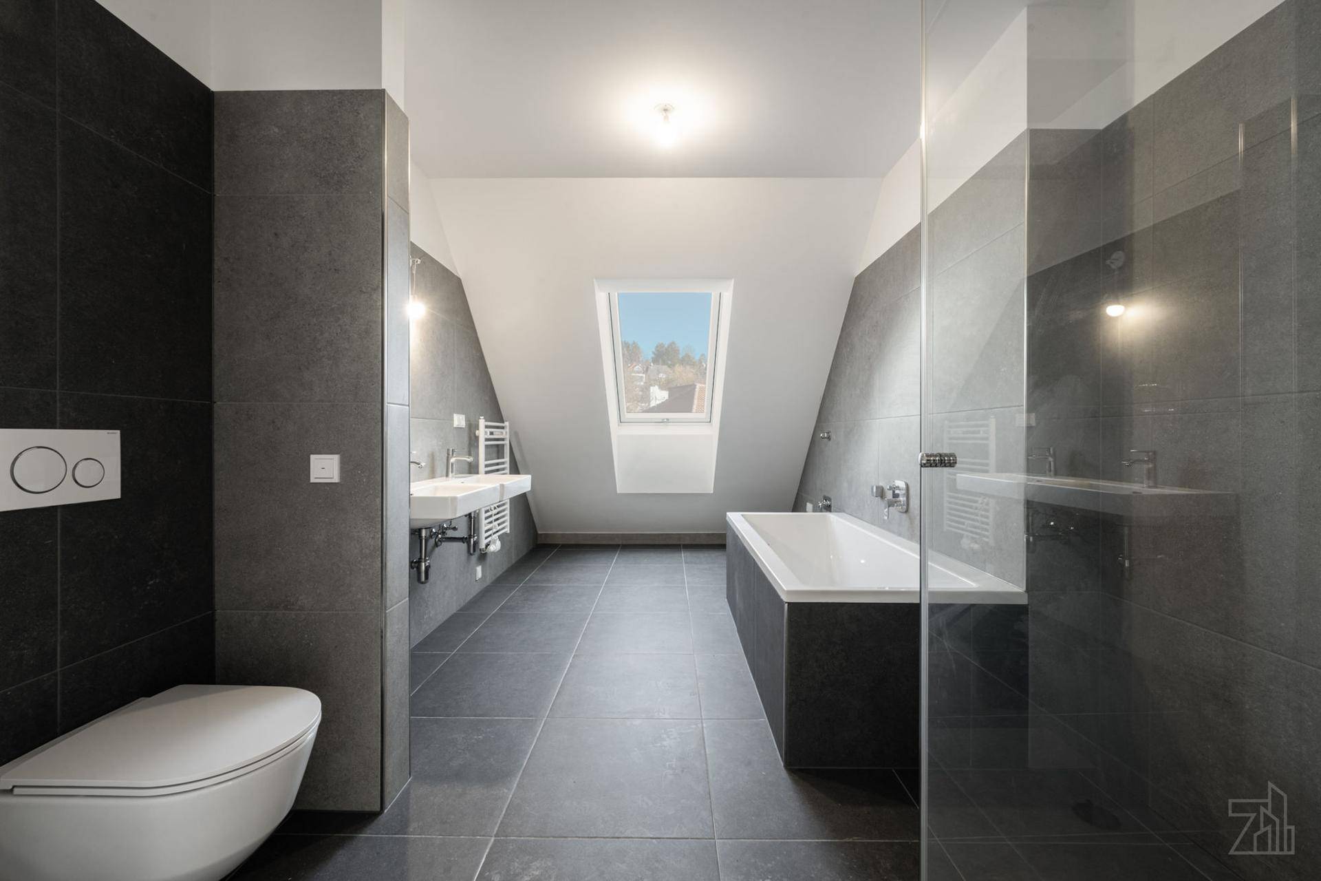 Modernes Badezimmer mit dunklen Fliesen, Badewanne, Doppelwaschbecken und Dachfenster.
