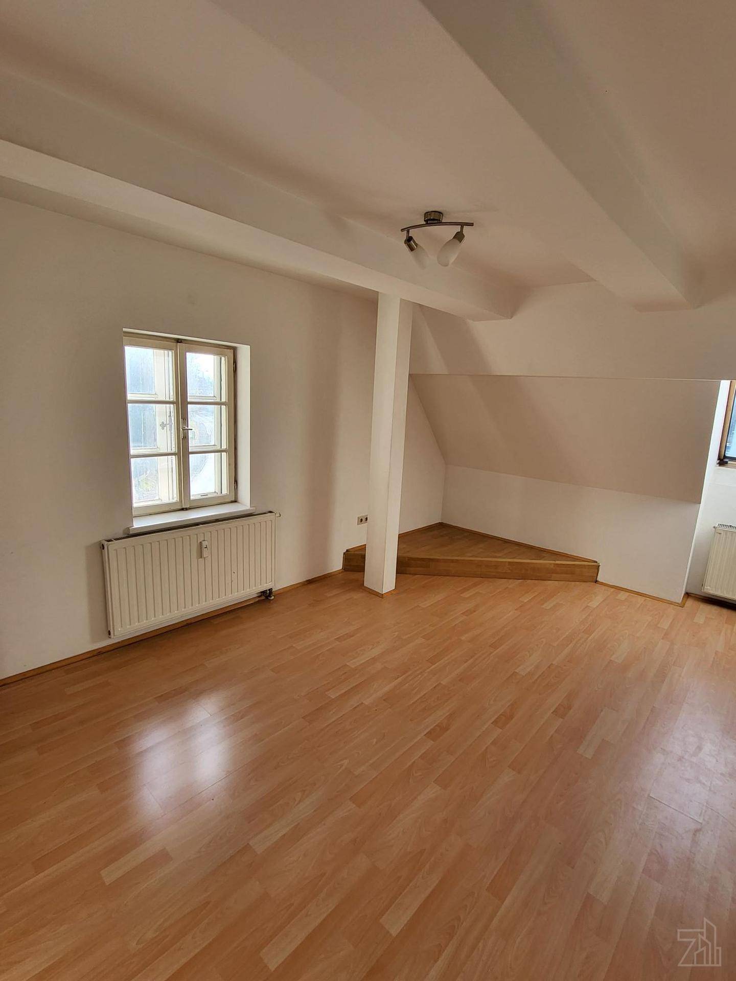 Geräumiger Dachbodenraum mit Holzboden, Dachschrägen und einem Fenster.