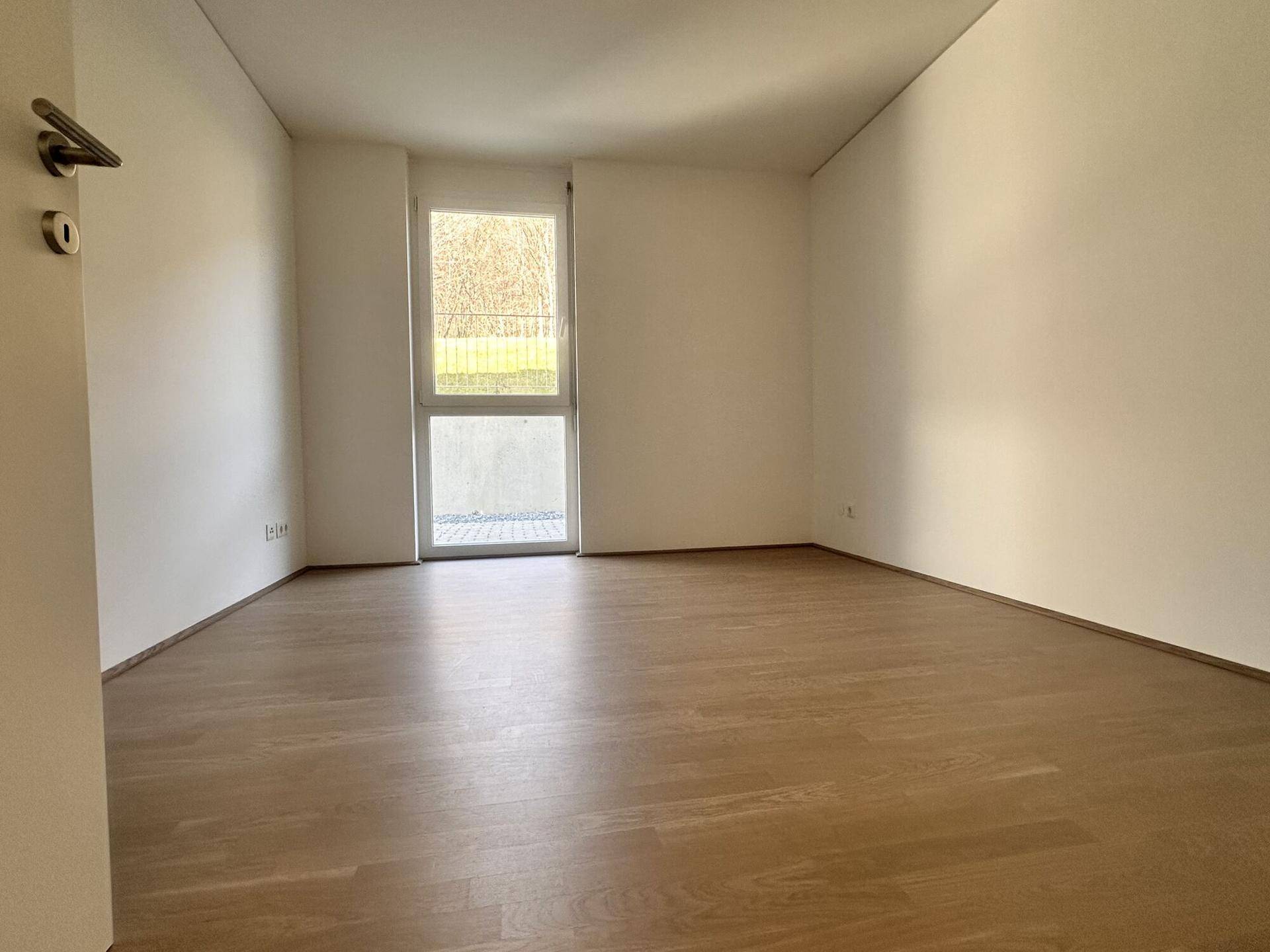 Helles Schlafzimmer mit Parkettboden und Fenster, das Zugang zum Außenbereich bietet.