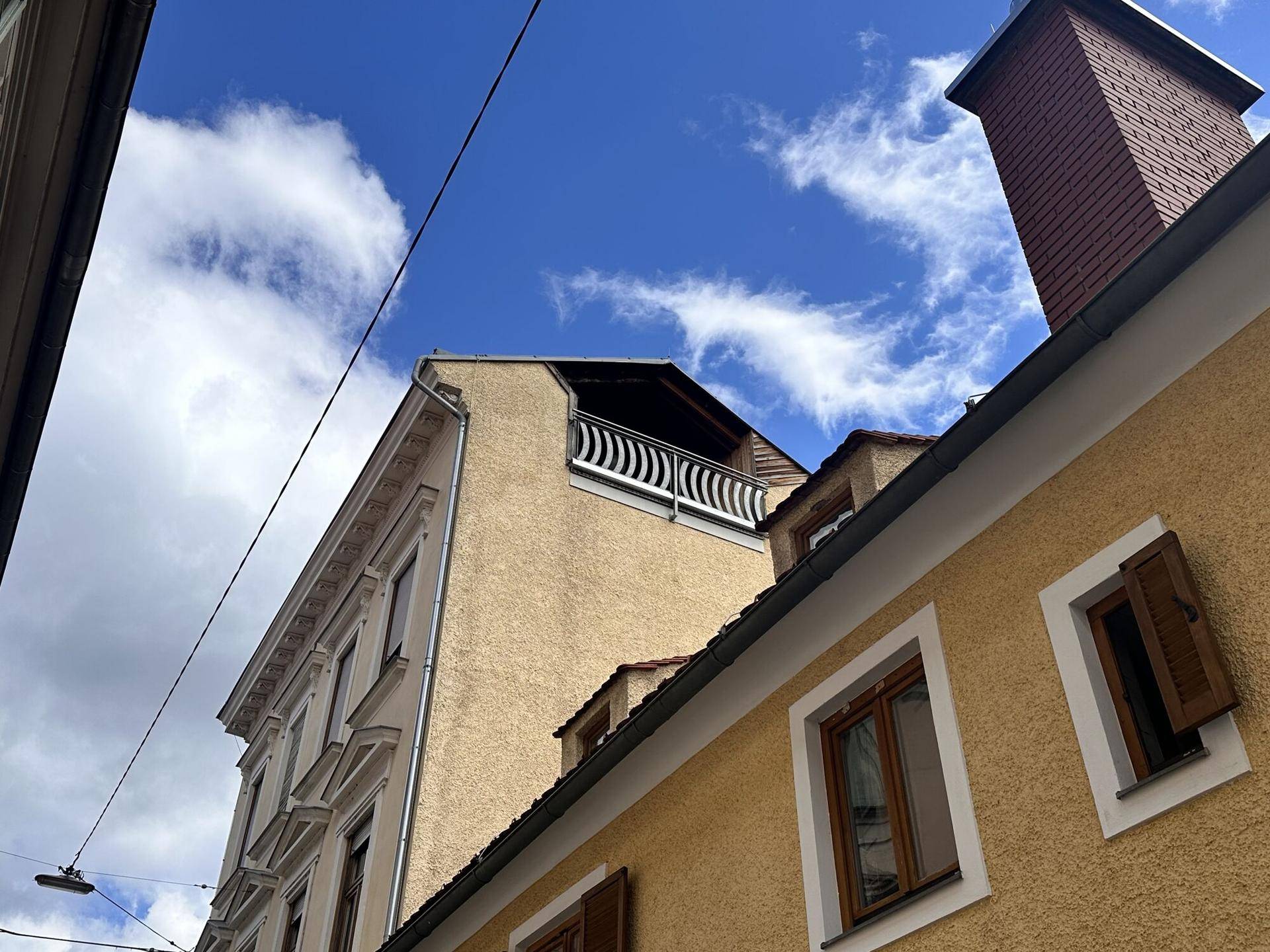 Historisches Gebäude mit einem Balkon im oberen Stockwerk unter blauem Himmel.