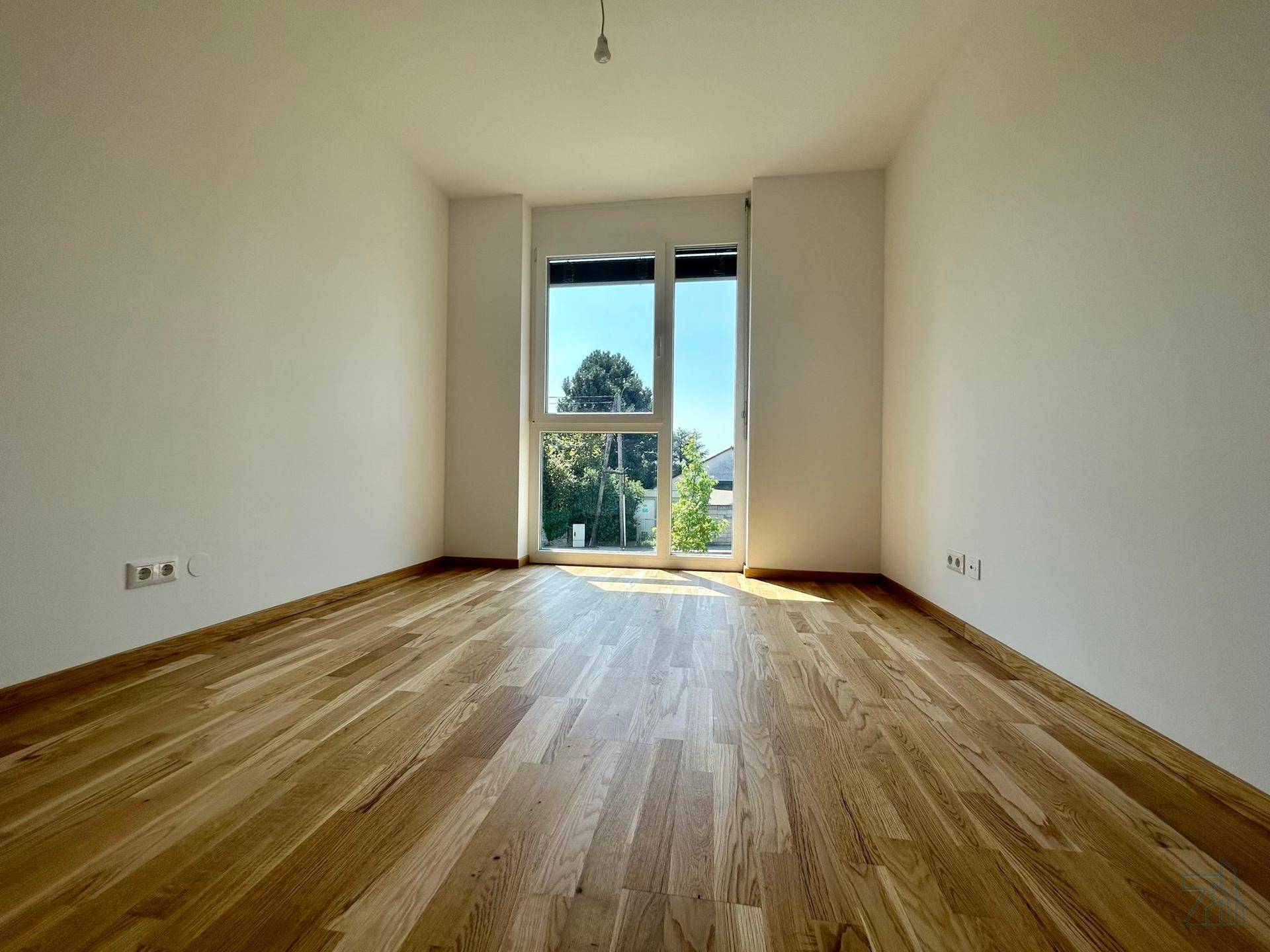 Helles Schlafzimmer mit Holzboden und großem Fenster mit Blick ins Grüne.
