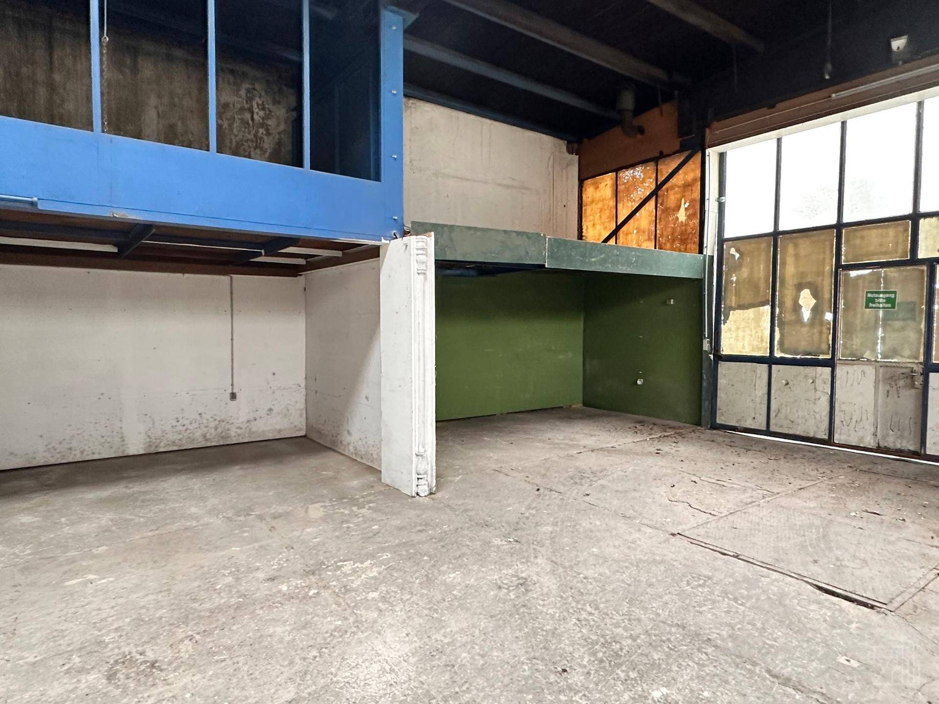 Ansicht des Lagerraums mit Mezzanine, grüner Wand und großen Fenstern am Eingangsbereich.