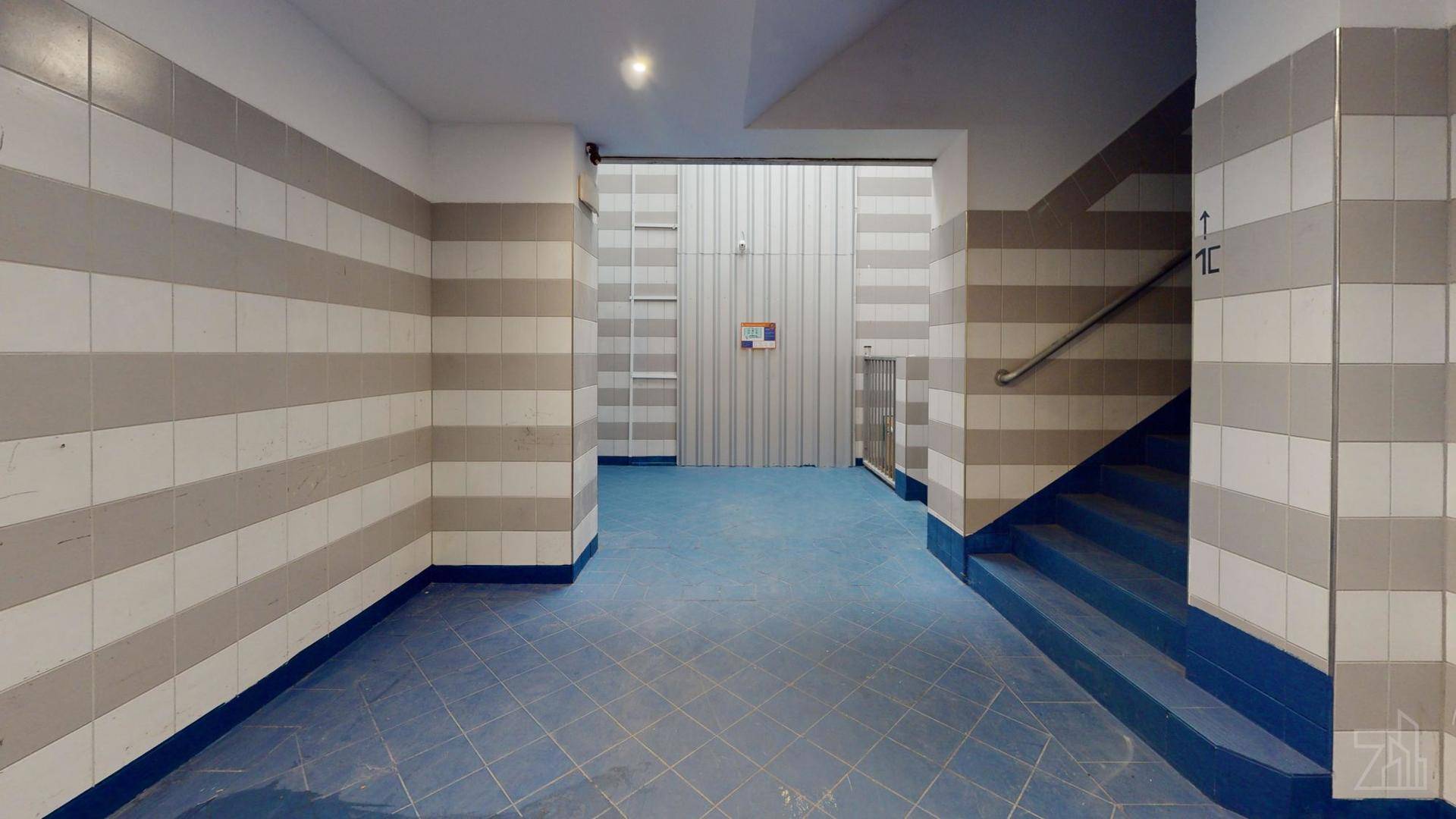 Gestreifter Flur mit grauen und weißen Fliesenwänden sowie einer Treppe mit blauem Boden.
