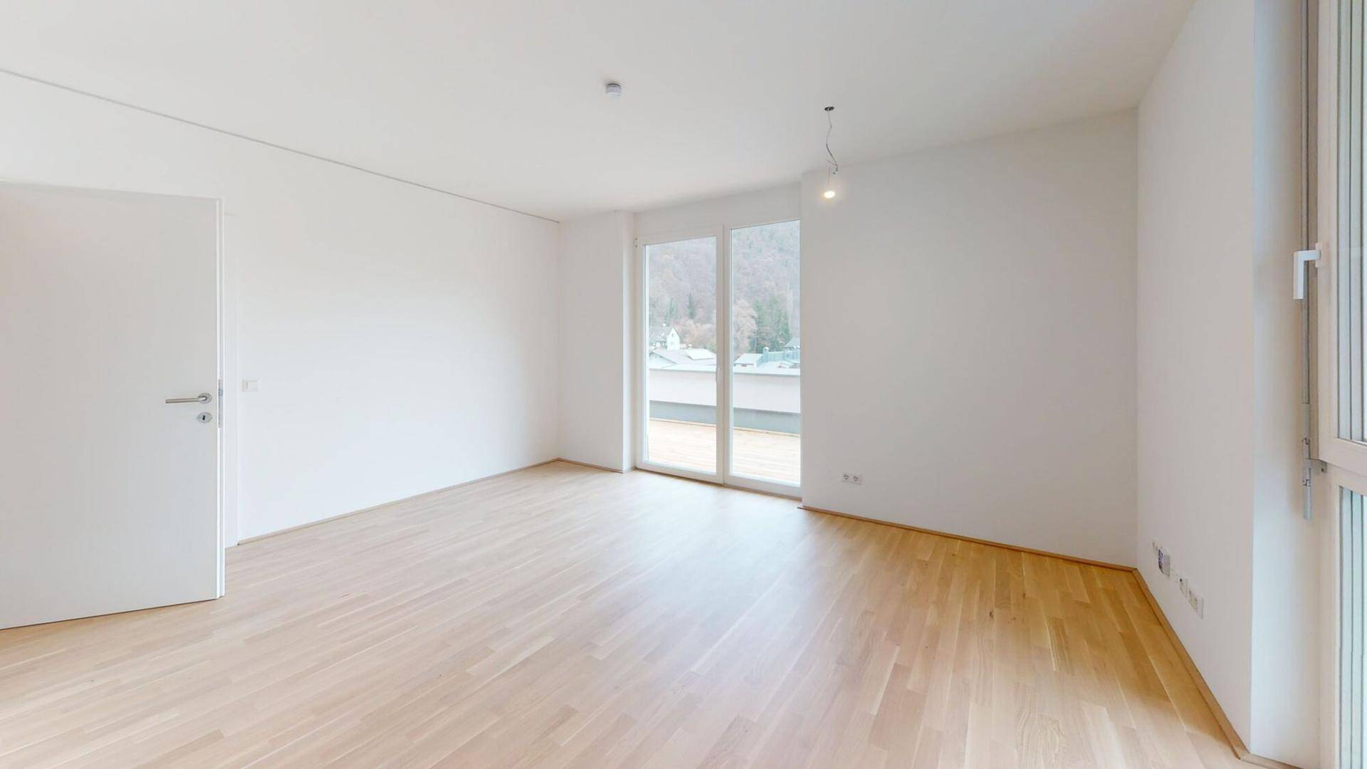 Geräumiger, heller Raum mit Holzboden und Zugang zu einem Außenbereich.