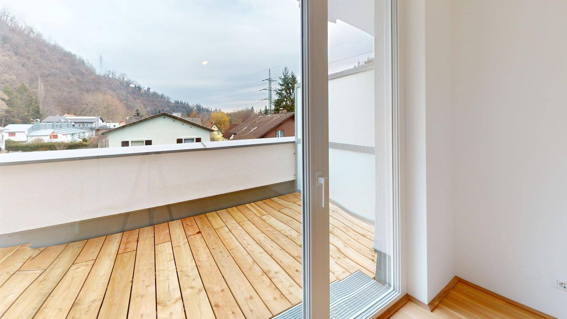 Geräumiger Balkon mit Holzdielen und Ausblick auf die umliegende Wohngegend und Hügel.