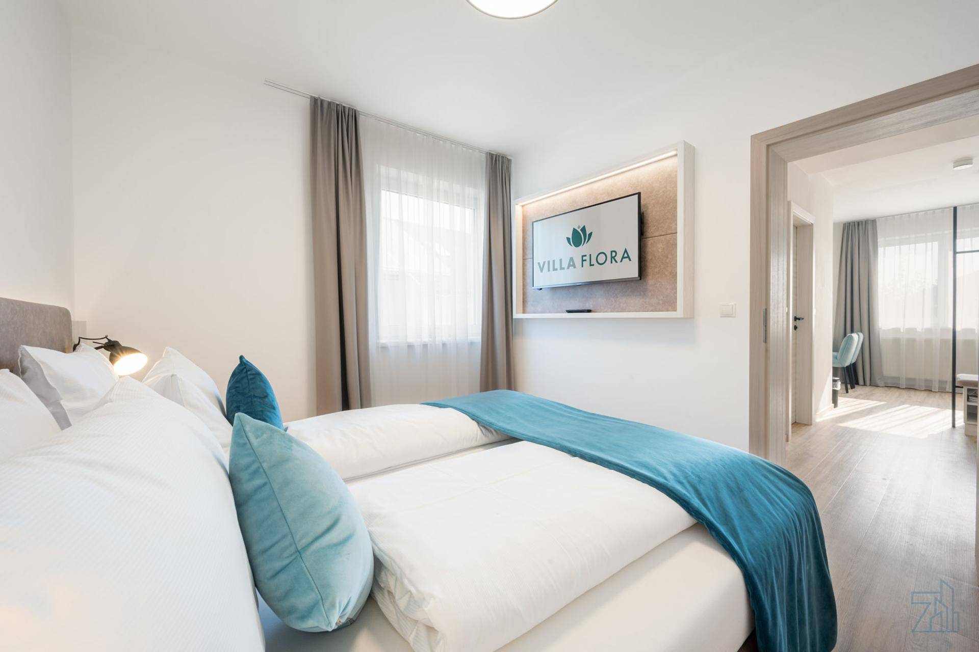 Helles Schlafzimmer mit Doppelbett, blauen Akzenten und einem modernen Wandfernseher.
