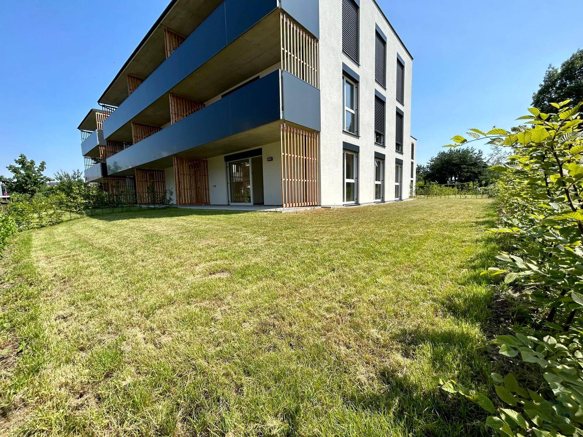 Modernes Mehrfamilienhaus mit weißer Fassade und großen Balkonen, umgeben von Grünflächen.