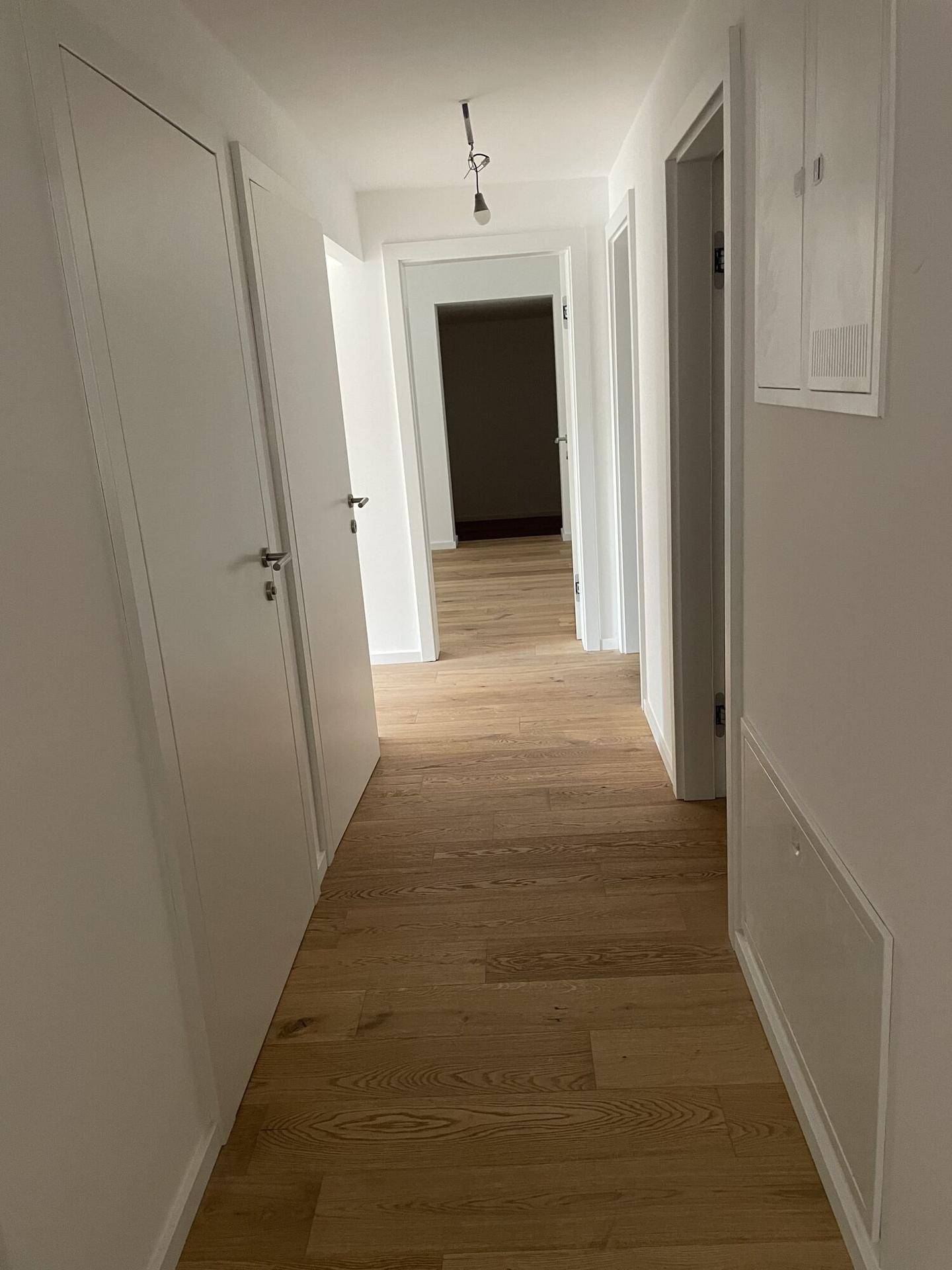 Heller Flur mit neuem Holzparkettboden und weißen Wänden, der zu weiteren Räumen führt.