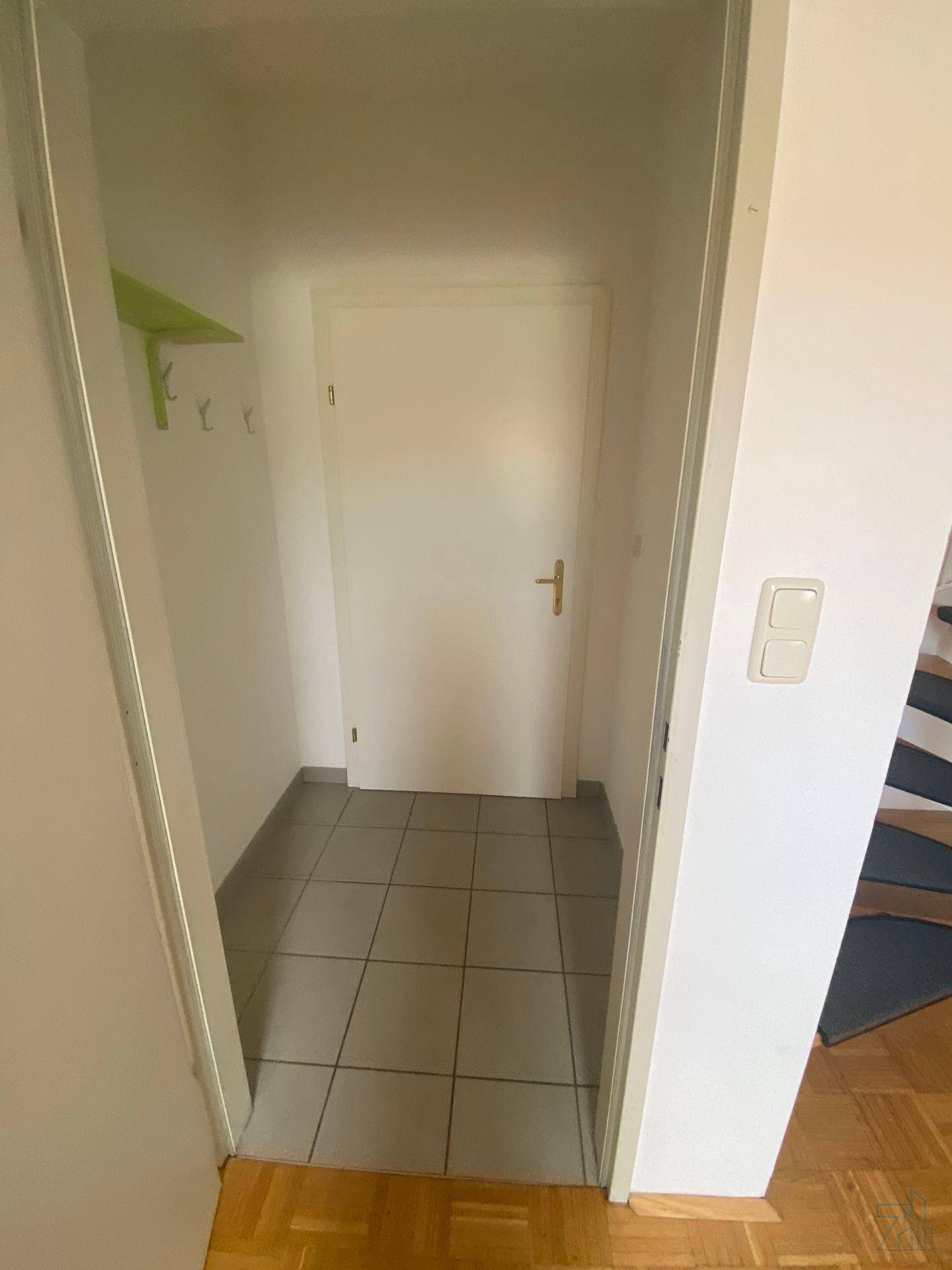 Kleiner Eingangsbereich mit Fliesenboden und Garderobenhaken an der Wand, praktisch für den Empfang.
