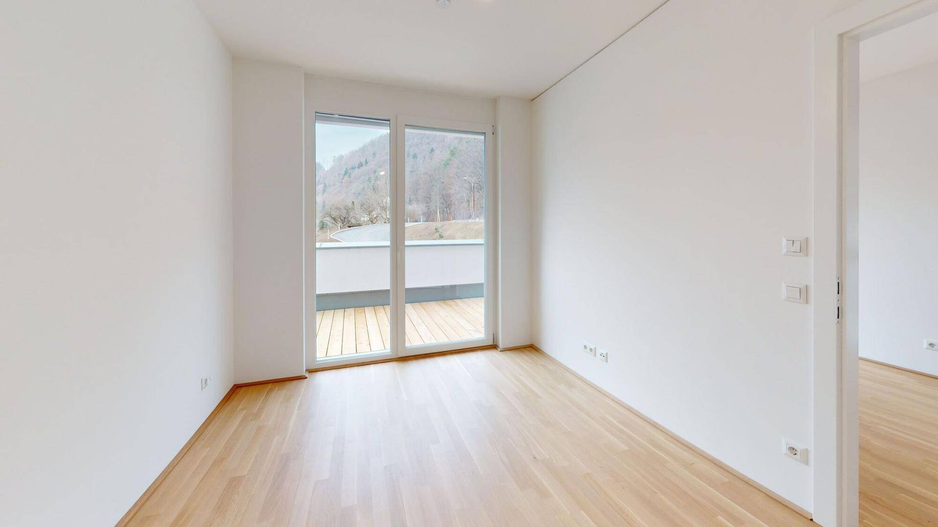 Leeres Zimmer mit Zugang zu einem Balkon und Blick auf die umliegende Berglandschaft.