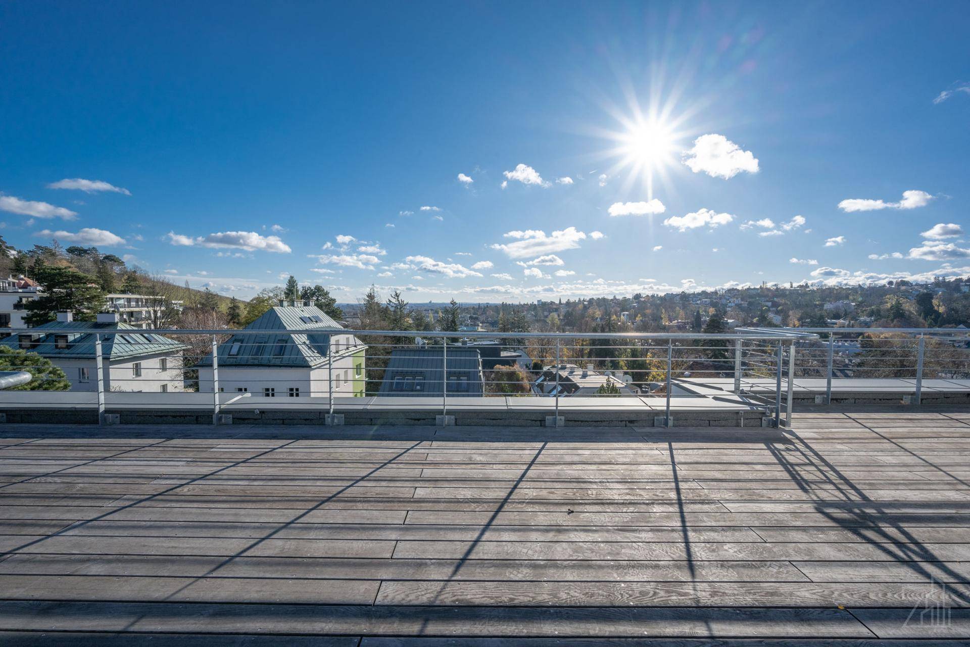 Weitläufige Dachterrasse mit Holzboden, Metallgeländer und Panoramablick unter strahlendem Himmel.