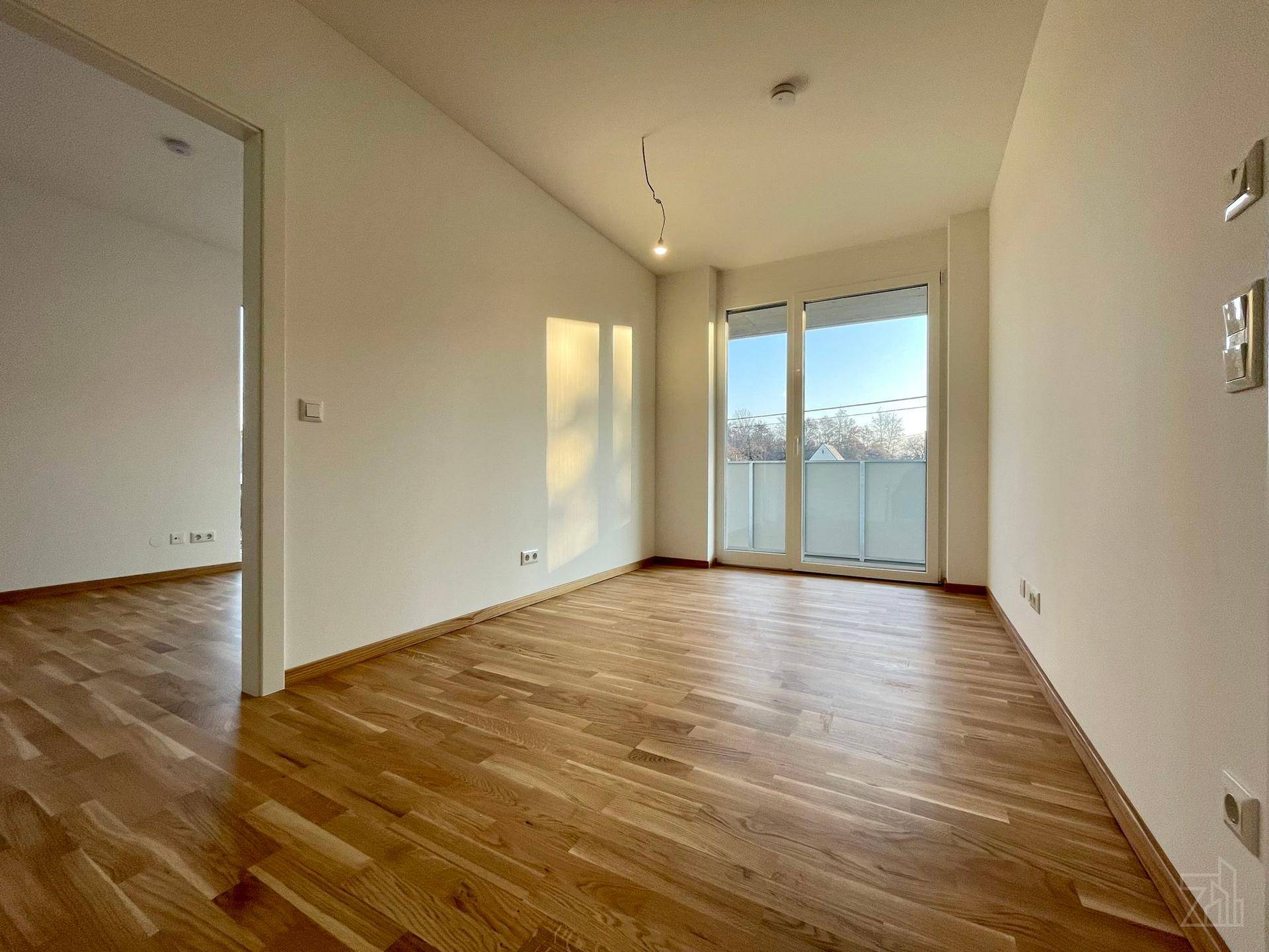 Geräumiger Wohnraum mit Holzboden und Schiebetür zum Balkon, hell und einladend.