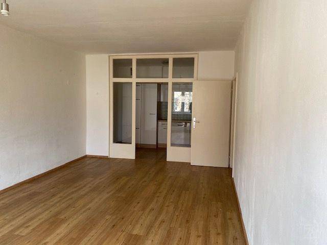 Geräumiges Wohnzimmer mit Laminatboden und Blick durch eine Glastür zur Küche.