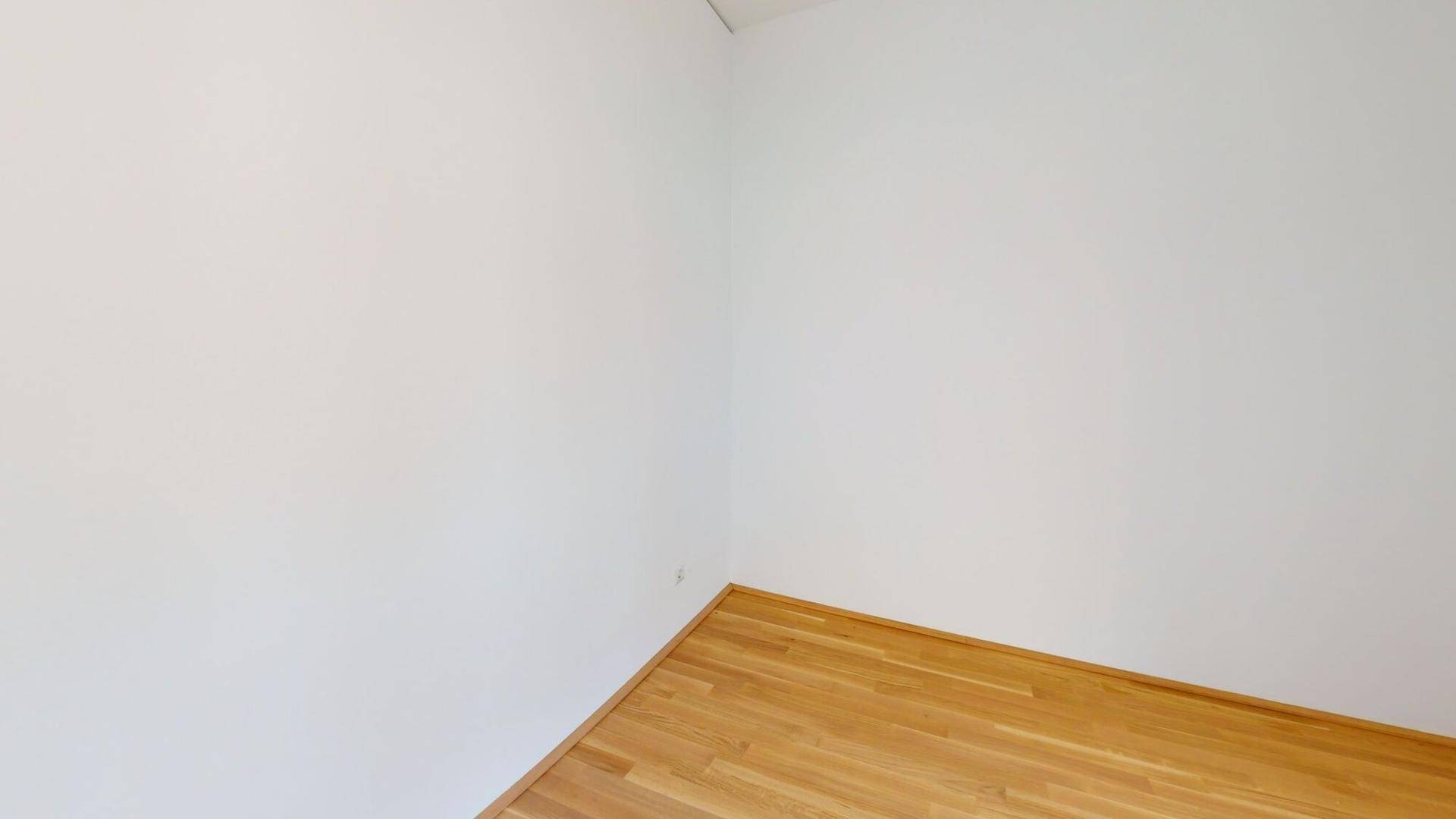Leere Ecke eines Raumes mit hellem Holzboden und weißen Wänden, bereit zur Einrichtung.