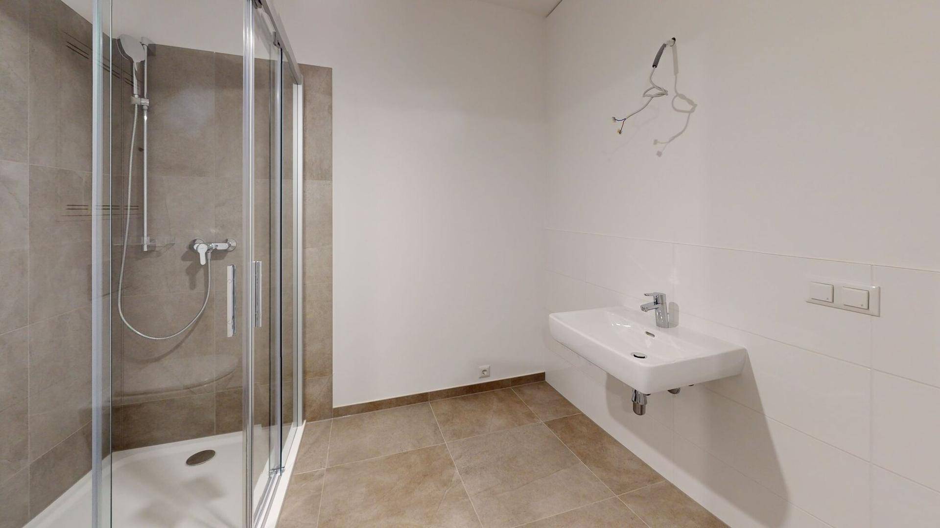 Helles Badezimmer mit moderner Duschkabine, Waschbecken und hellbraunen Fliesen.