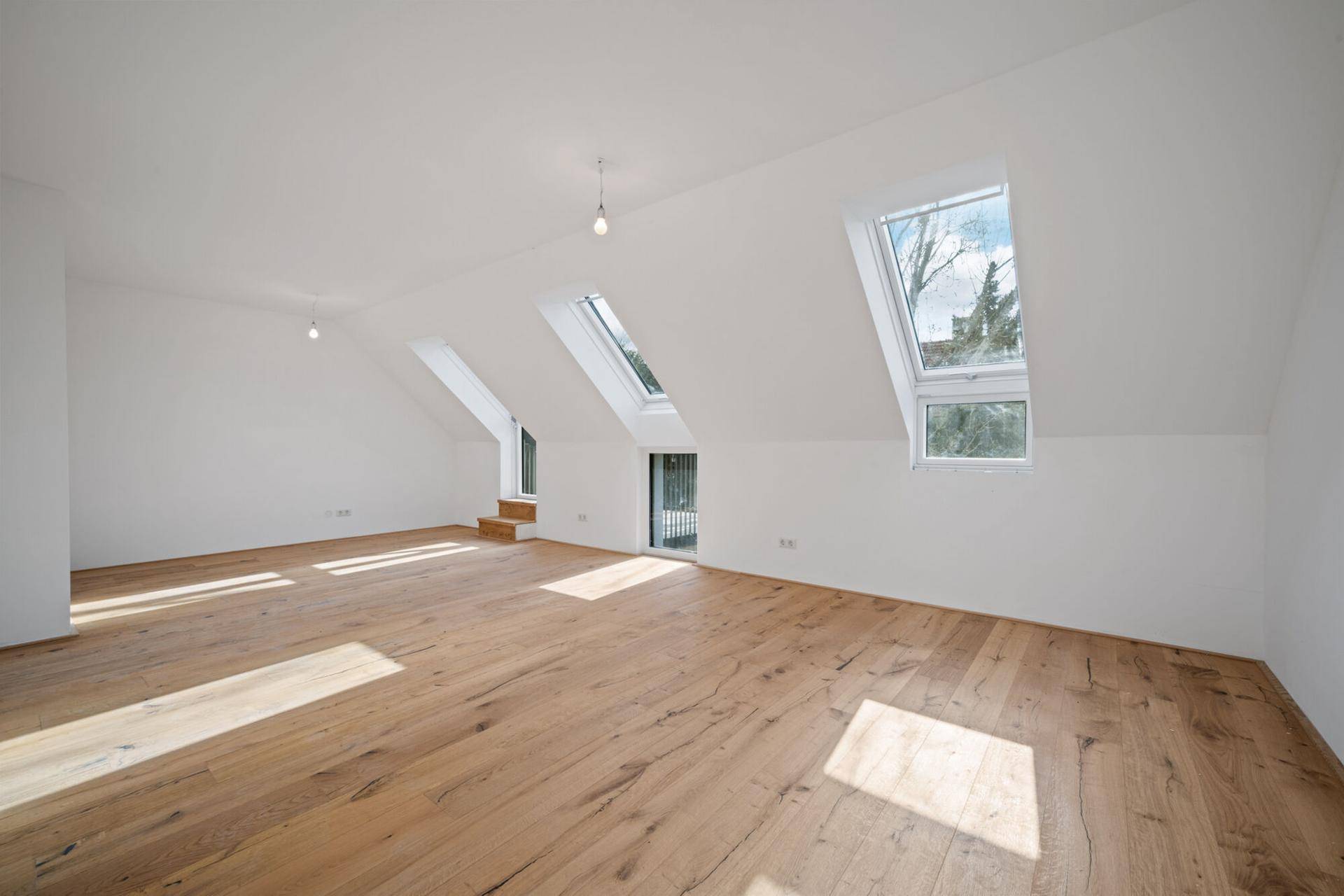 Helles, geräumiges Zimmer im Dachgeschoss mit Holzboden und großen Dachfenstern.