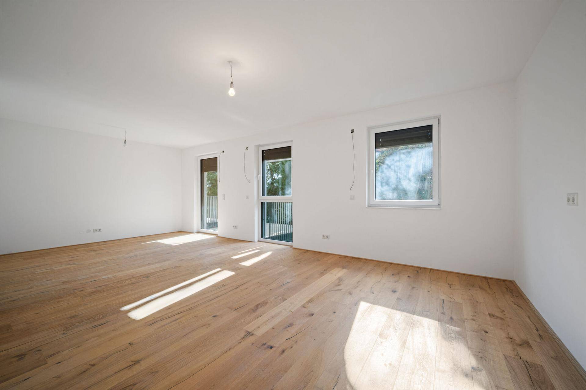 Helles, leeres Zimmer mit Echtholz-Dielenboden und Zugang zu einem Balkon oder einer Terrasse.