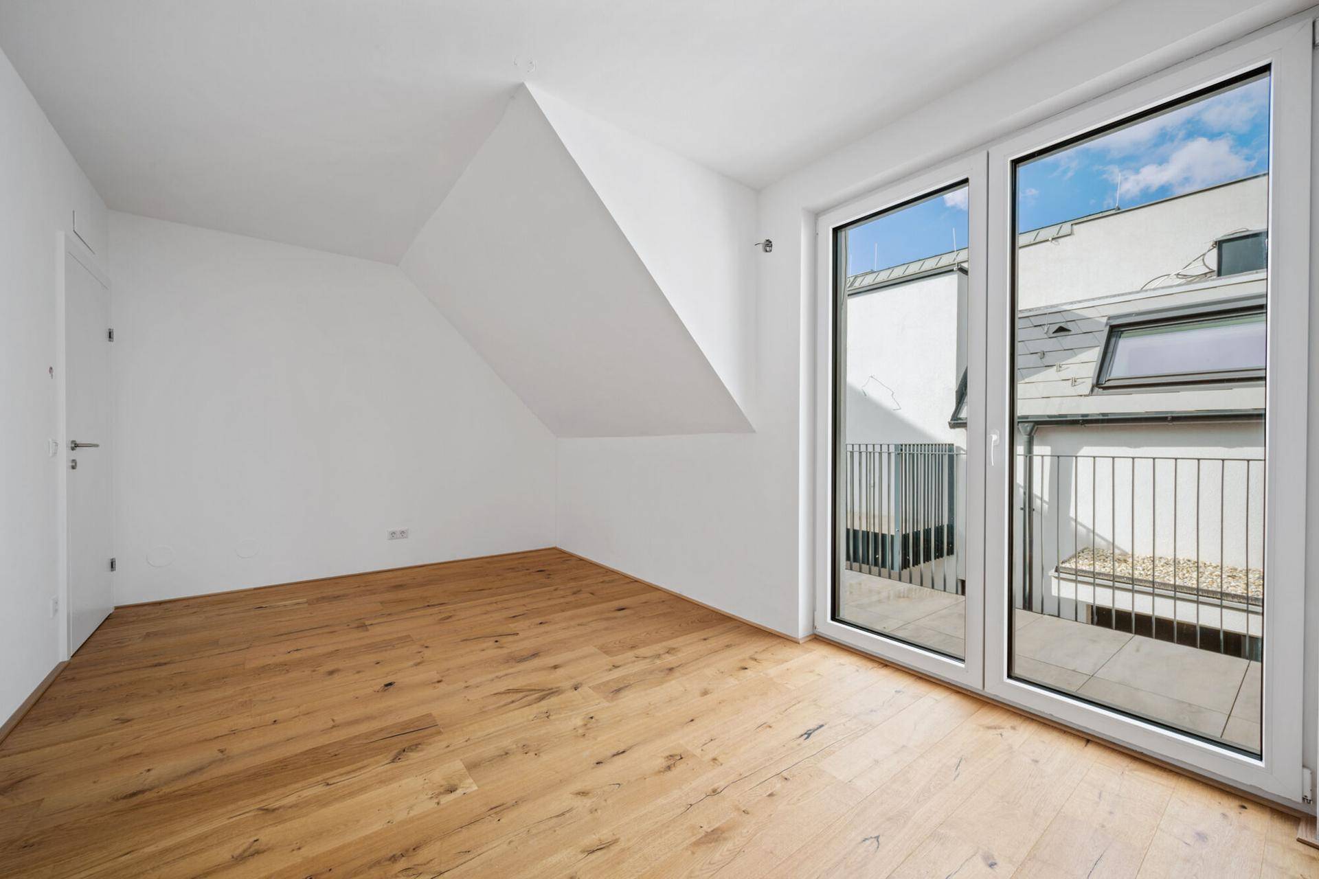 Helles Schlafzimmer mit Holzboden, Dachschräge und Zugang zu einem kleinen Balkon.