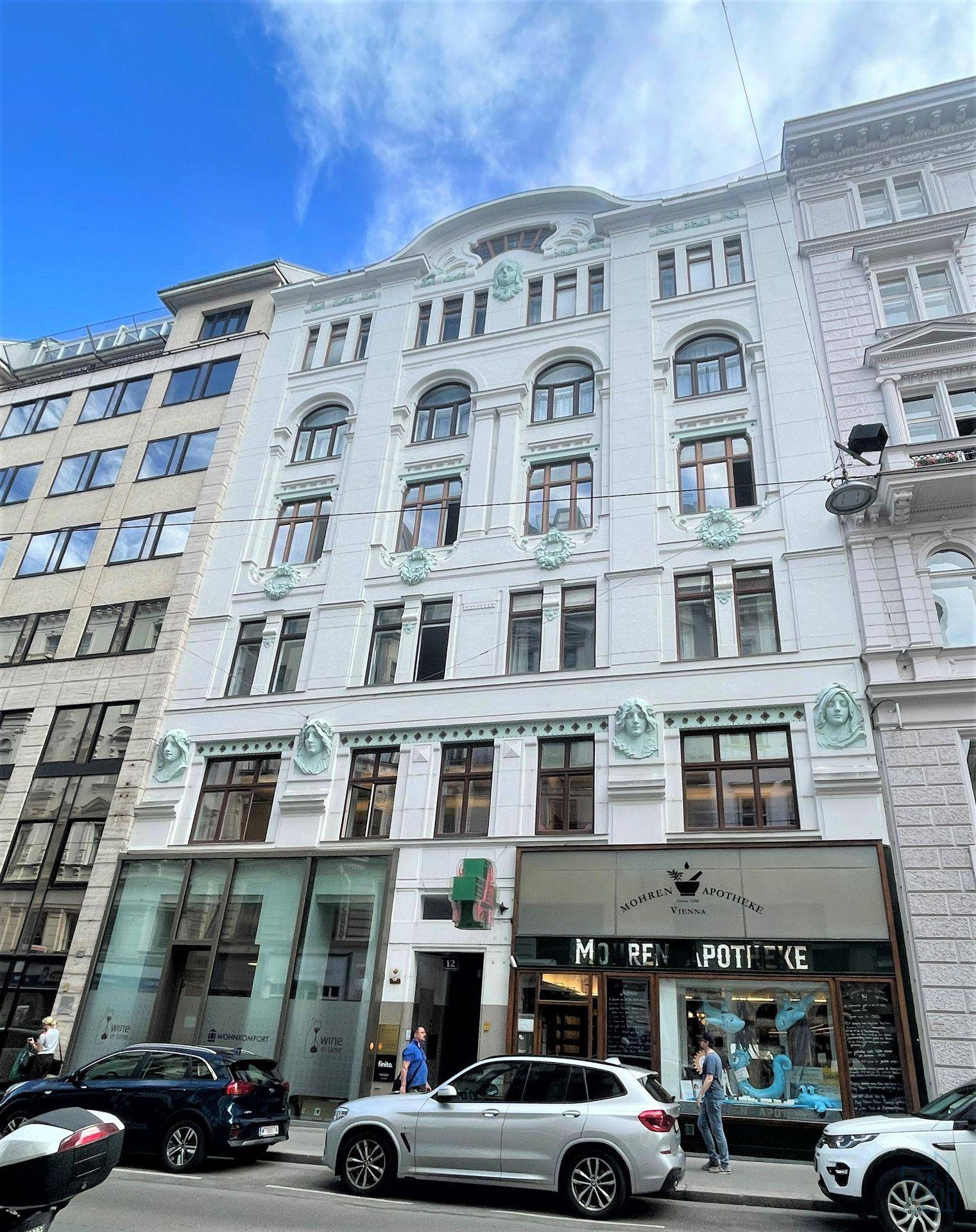 Historische Fassade eines Gebäudes mit kunstvollen Verzierungen in einer belebten Stadtstraße.