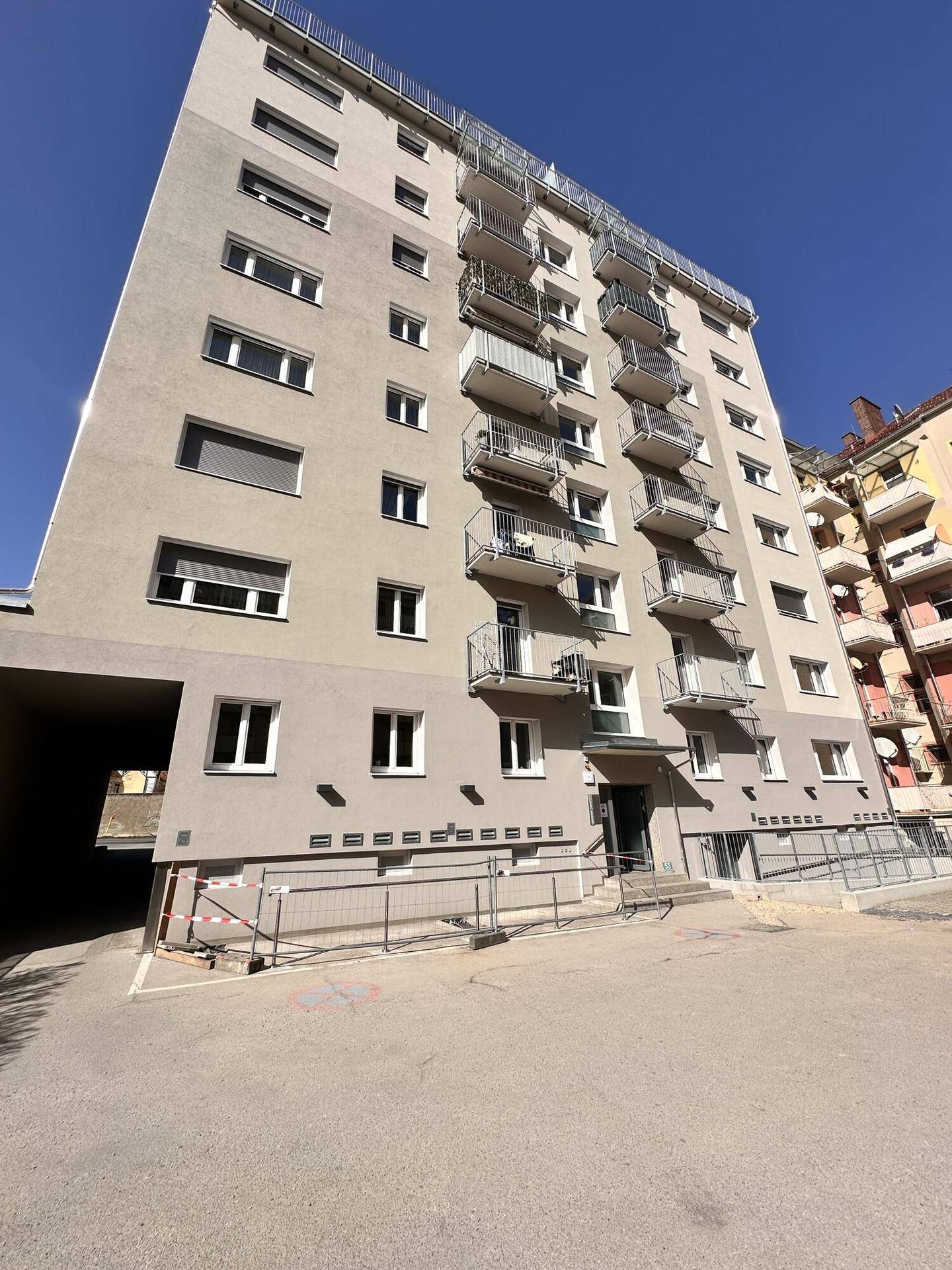 Hohes Mehrfamilienhaus mit vielen Balkonen und einer Rampe am Eingangsbereich.