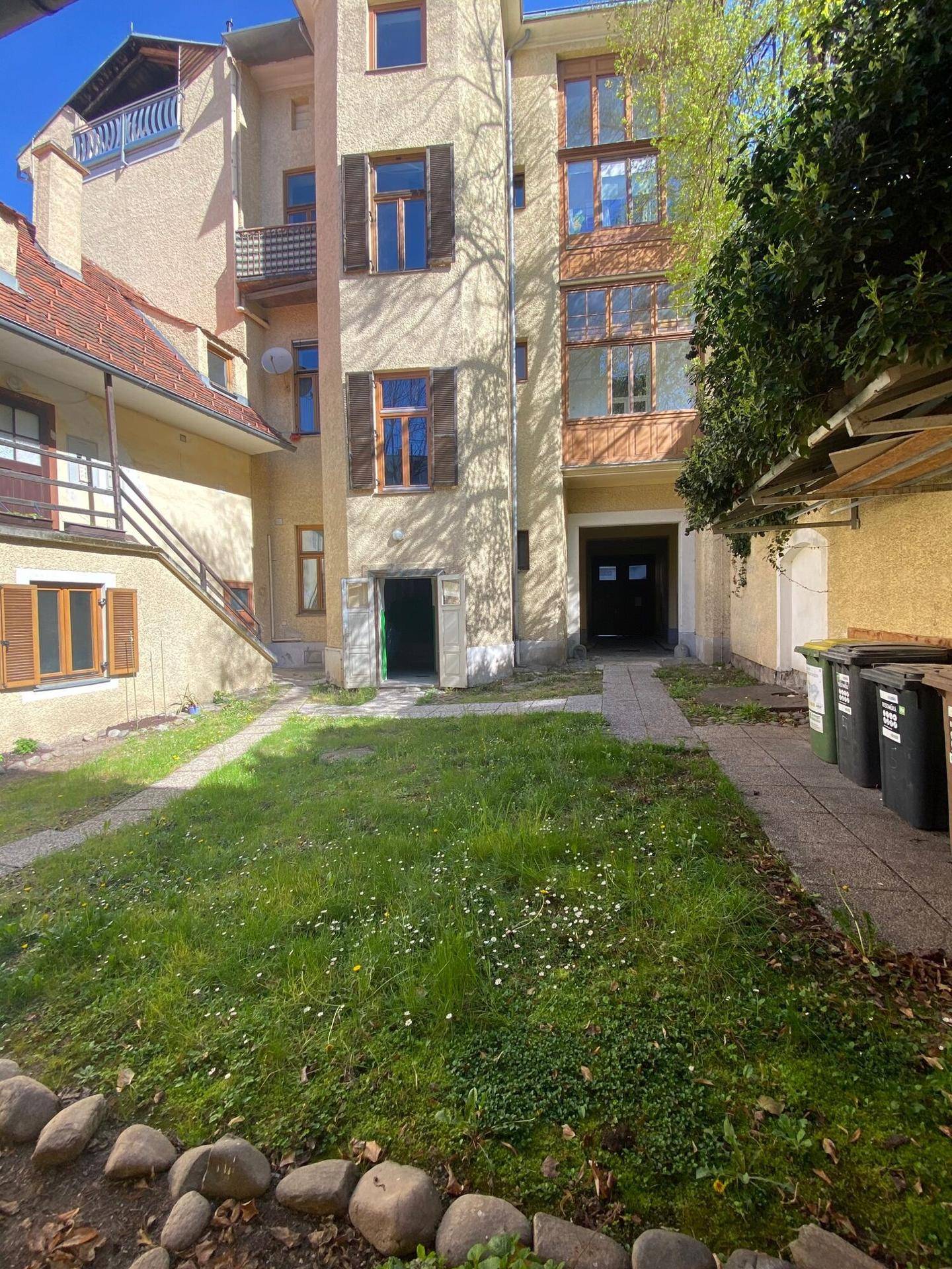 Hinterhof mit Rasenfläche und Zugang zu den Gebäuden, umgeben von alten Mauern.