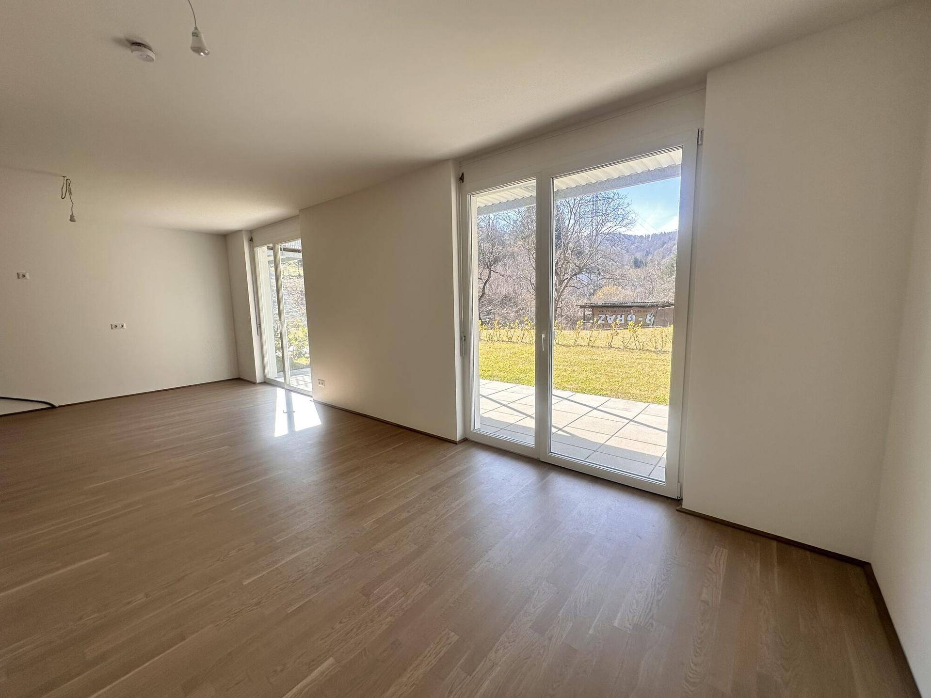 Geräumiges Wohnzimmer mit hellem Parkettboden und direktem Zugang zur Terrasse und zum Garten.