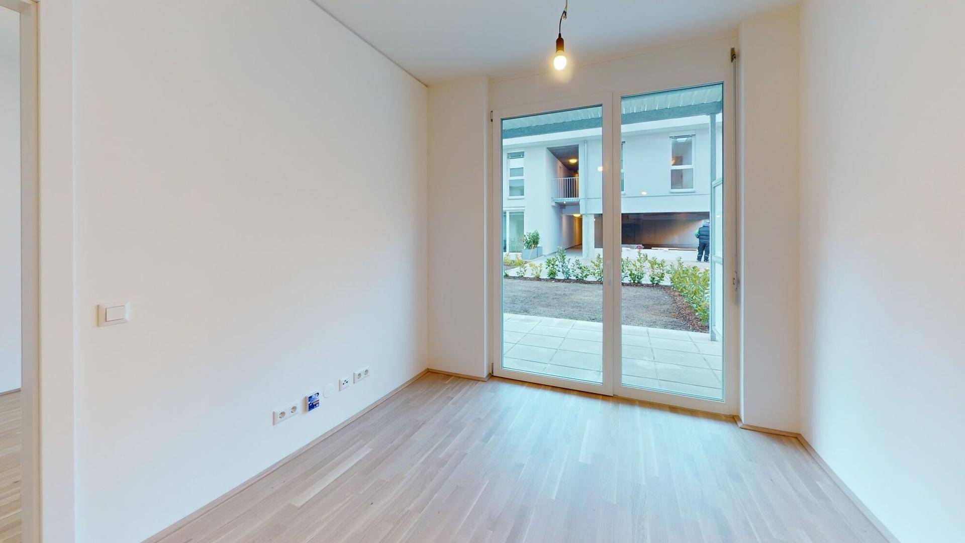 Helles Zimmer mit Parkettboden und großen Fenstern, die viel Tageslicht hereinlassen.
