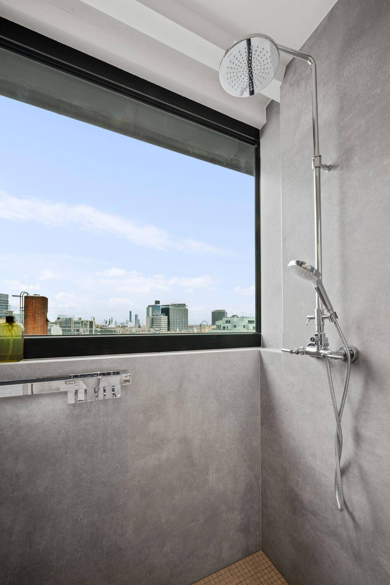 Moderne Dusche mit Regenduschkopf und großem Fenster mit Panoramablick auf die Stadt.