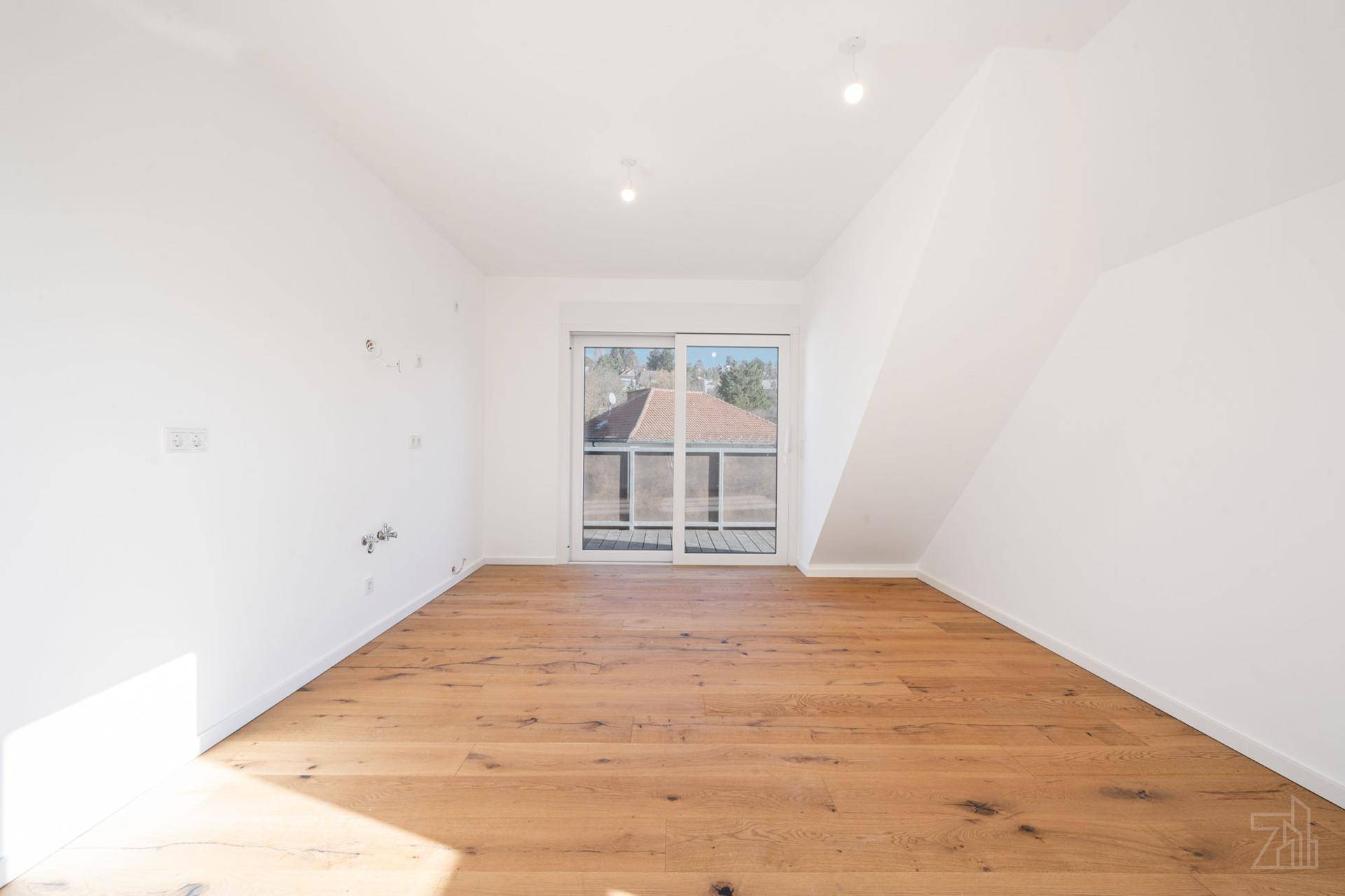 Heller Raum mit Holzboden, Schiebetür zum Balkon und schrägen Wänden im Dachgeschoss.