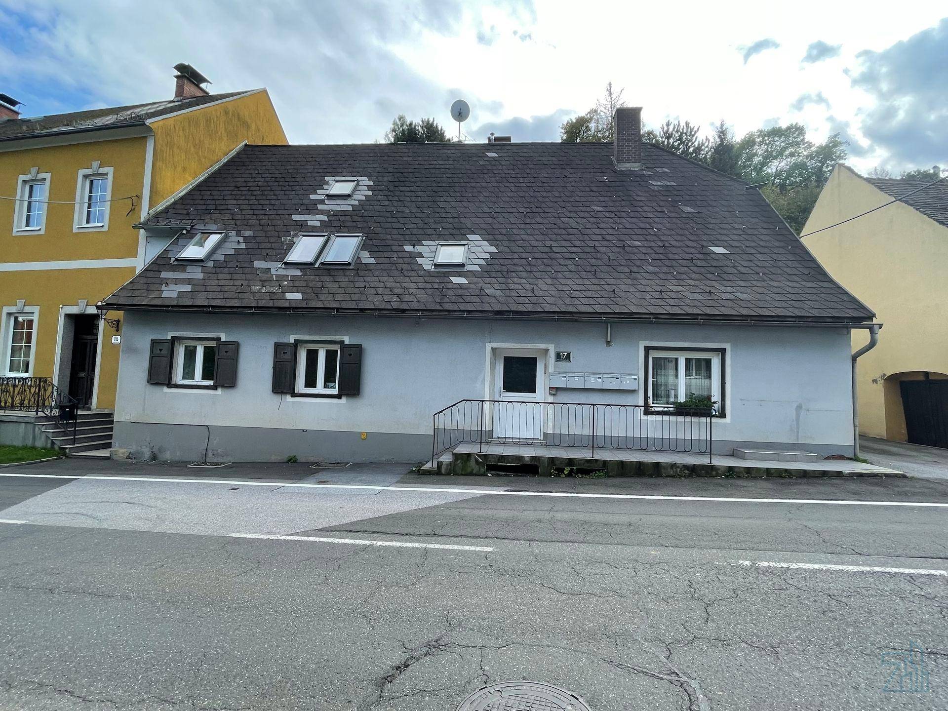 Ansicht eines älteren Wohnhauses mit grauer Fassade und traditionellem Satteldach.