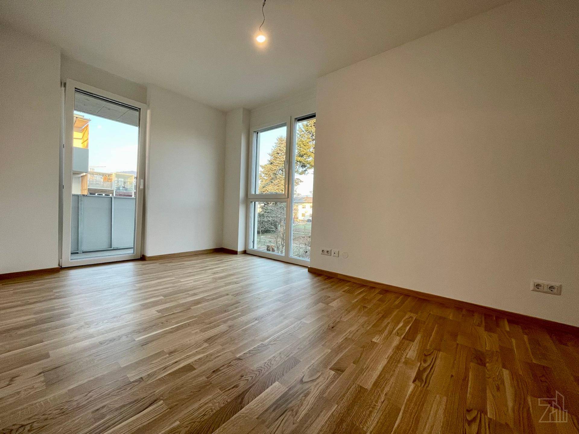 Heller Wohnraum mit Holzboden, großen Fenstern und Zugang zu einem Balkon.
