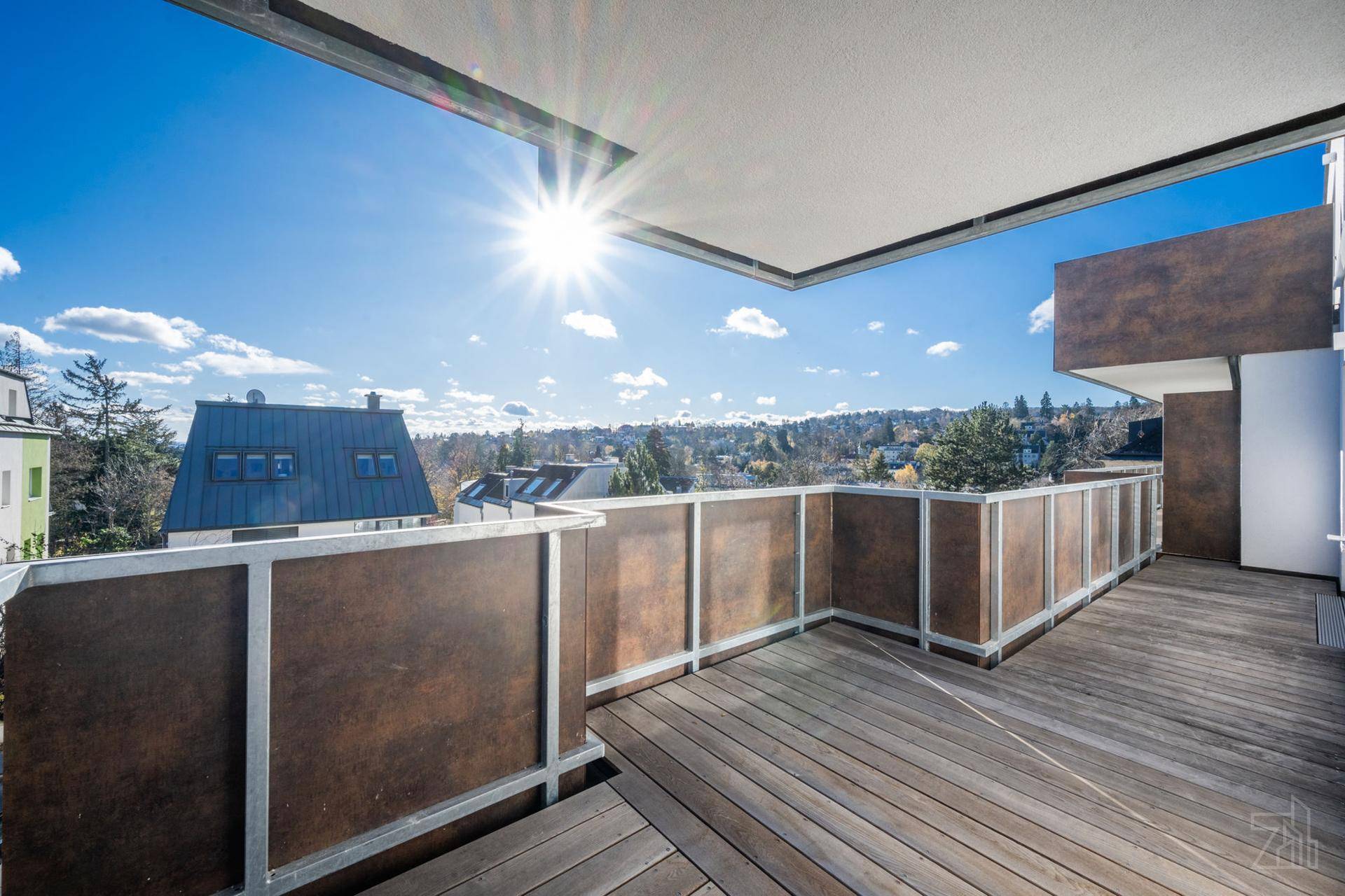 Großer sonniger Balkon mit Holzboden und weitem Blick über die umliegende Landschaft.