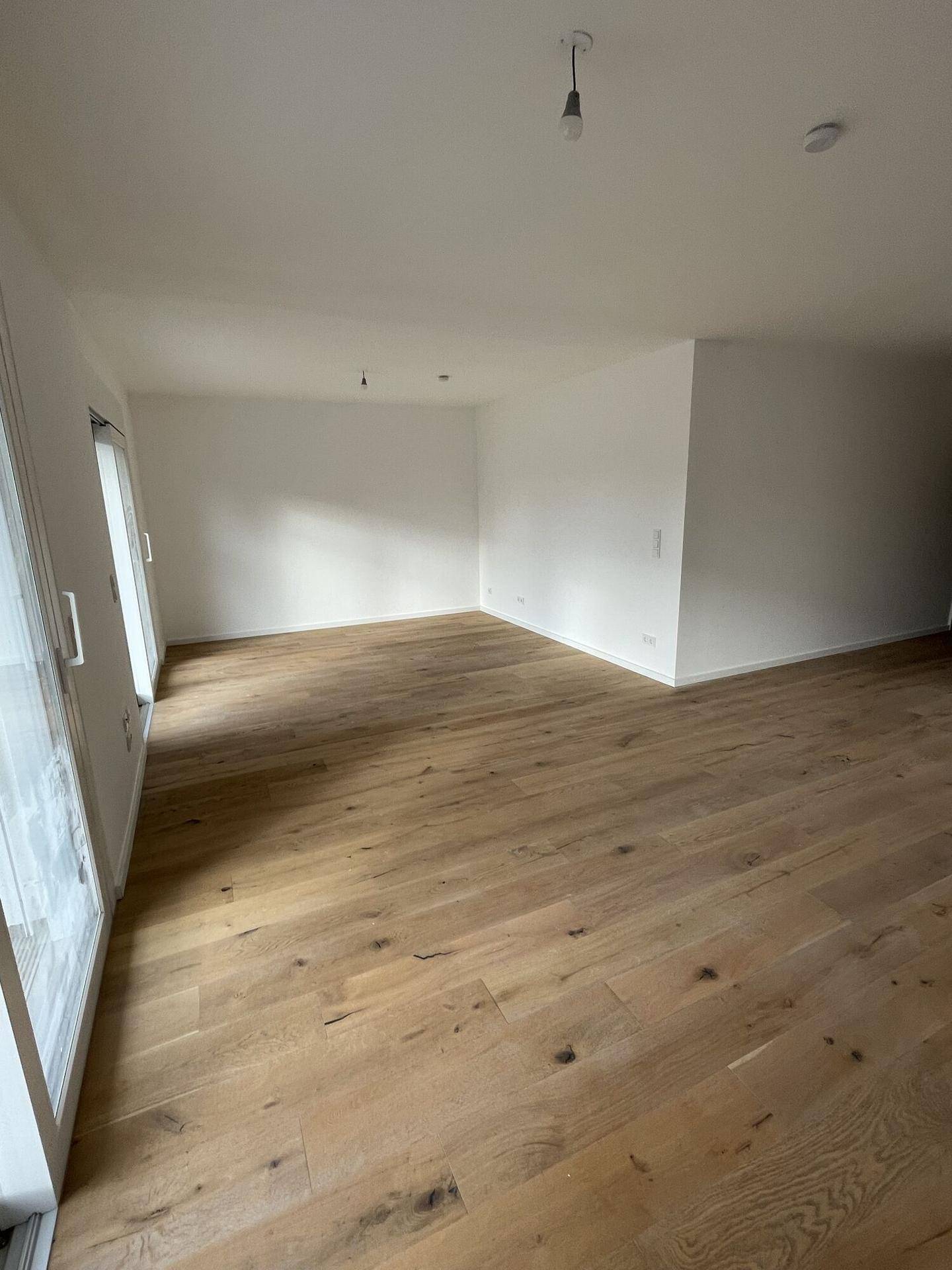 Heller, leerer Raum mit großen Fenstern und neuem Holzparkettboden, bereit zur individuellen Gestaltung.