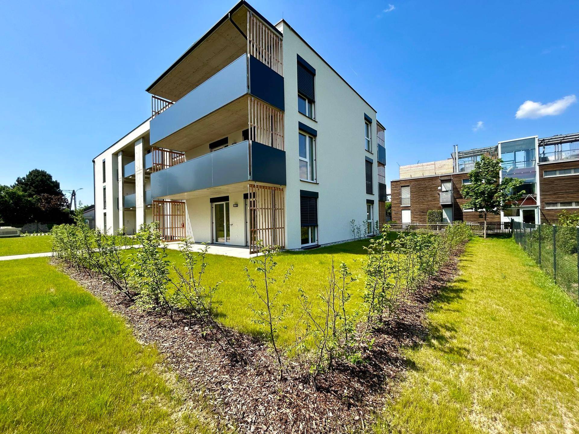Seitenansicht eines modernen Apartmentgebäudes mit Balkonen und frisch angelegten Hecken im Gartenbereich.
