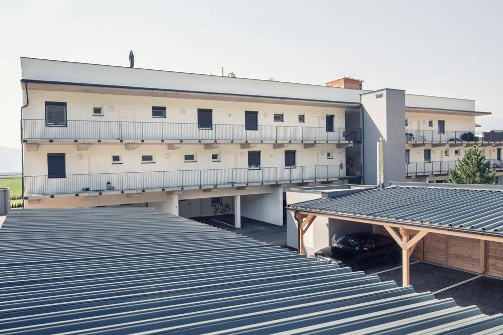 Modernes Wohngebäude mit mehreren Balkonen, Carports und Parkplätzen im Freien.