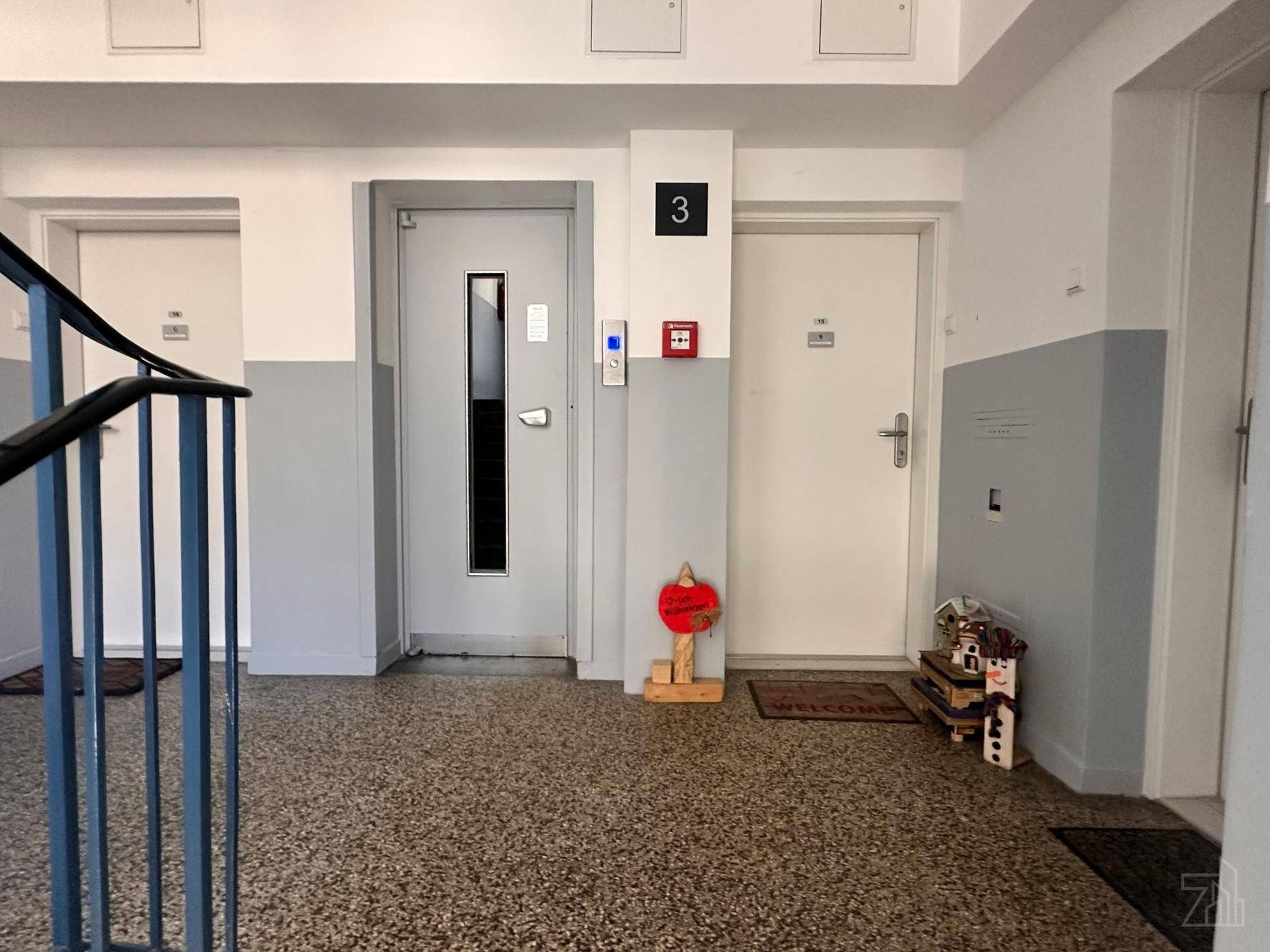 Flur mit Aufzug und Wohnungstüren, dekoriert mit kleinen Willkommensschildern.