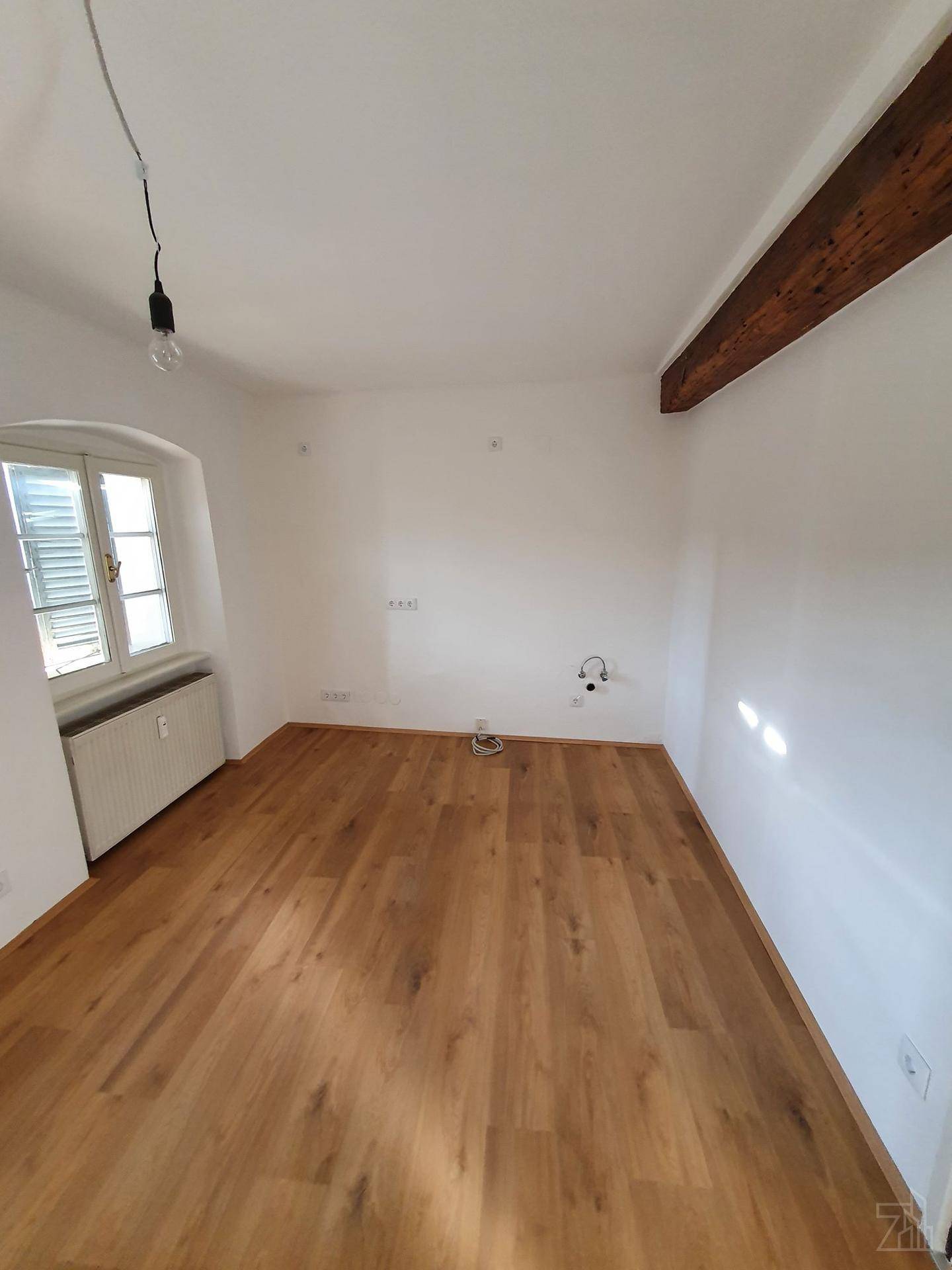 Heller Raum mit Holzbalken, Parkettboden und einem Fenster mit Blick nach draußen.