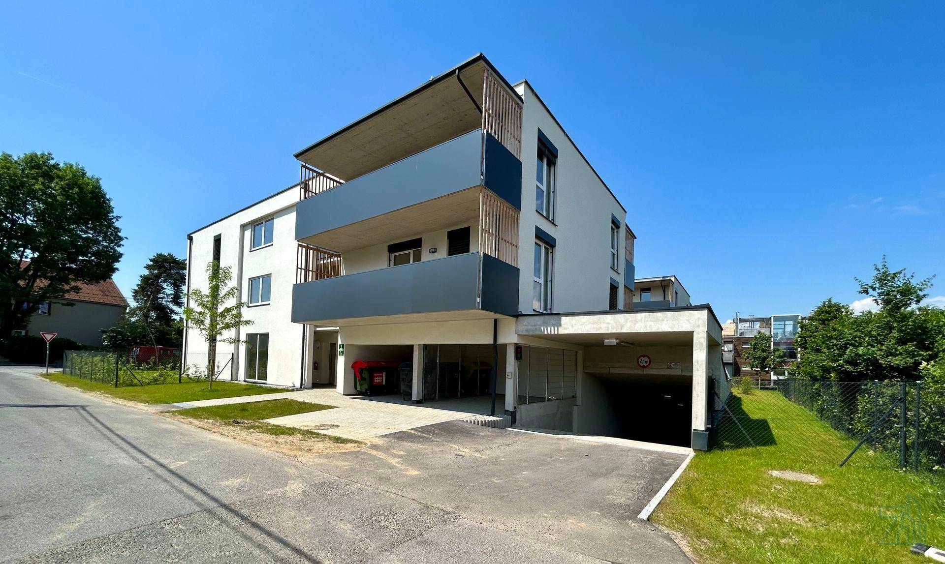 Modernes Wohngebäude mit Tiefgaragenzufahrt und Balkonen unter strahlend blauem Himmel.