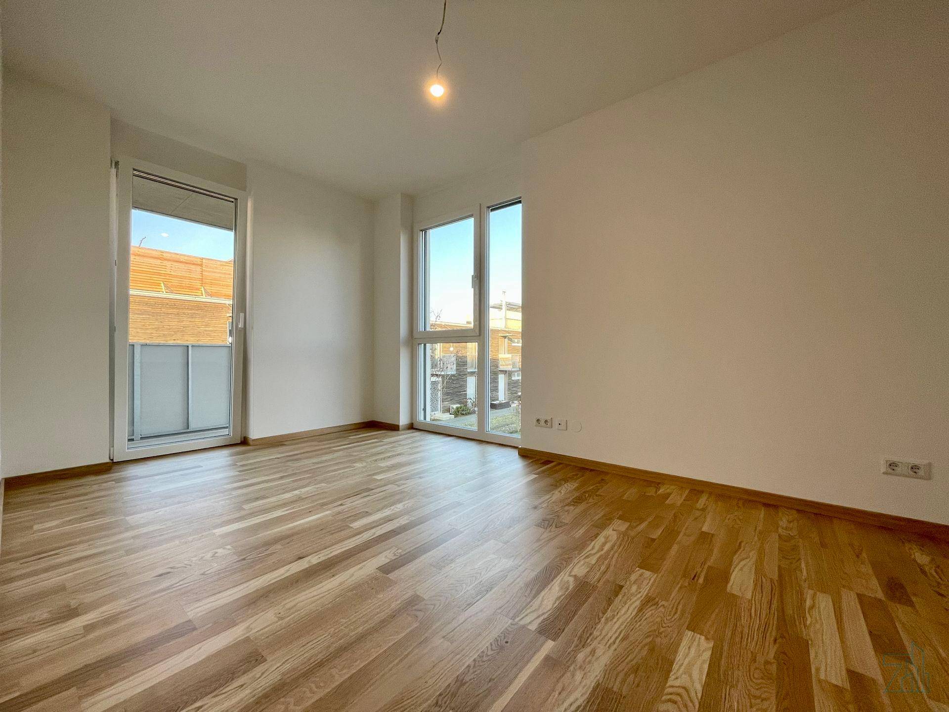 Geräumiger, heller Raum mit großen Fenstern und Zugang zu einem Balkon, ausgestattet mit Parkettboden.