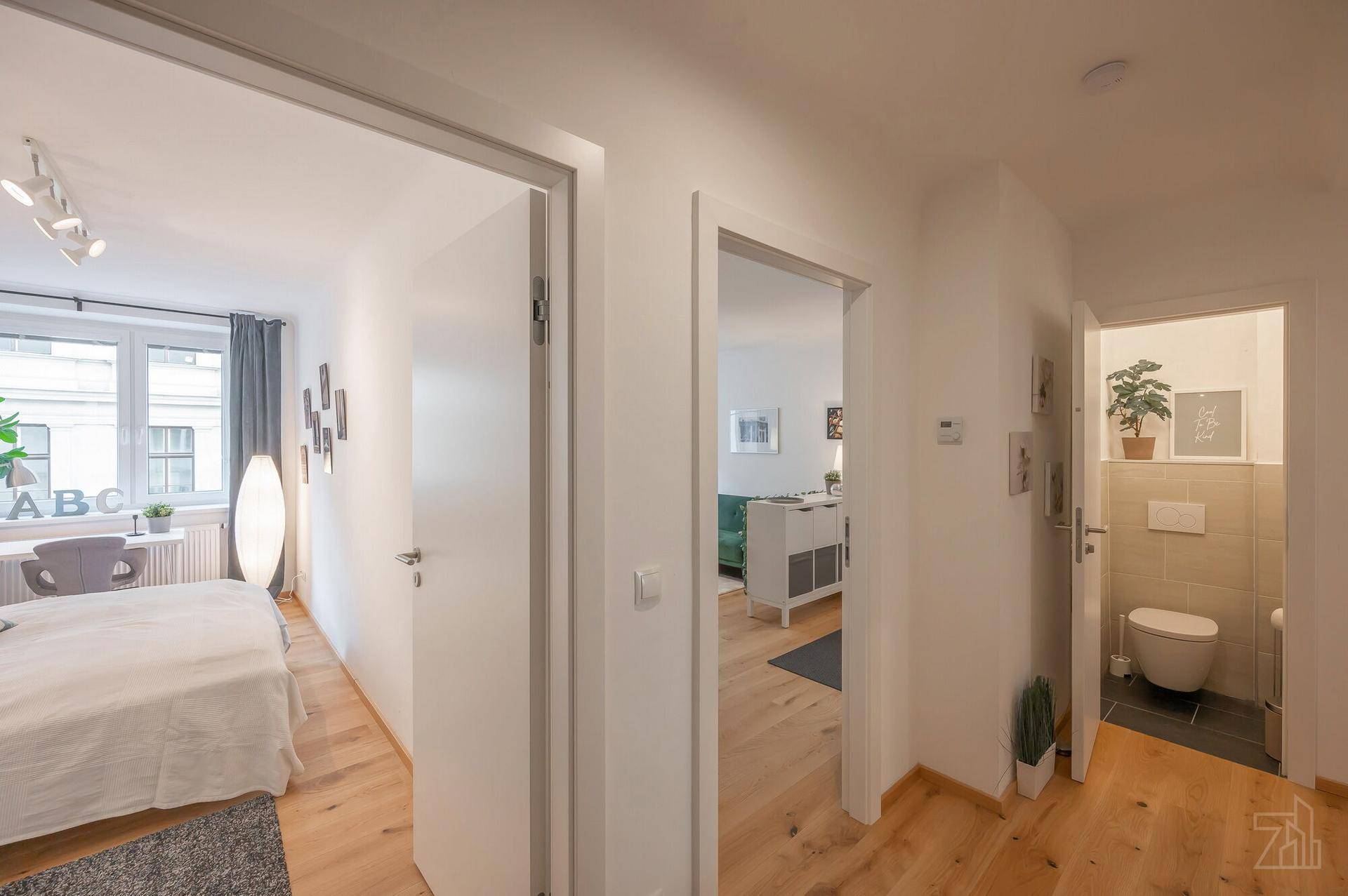 Heller Flur mit Holzboden, der zu verschiedenen Zimmern führt, inklusive Schlafzimmer und WC.