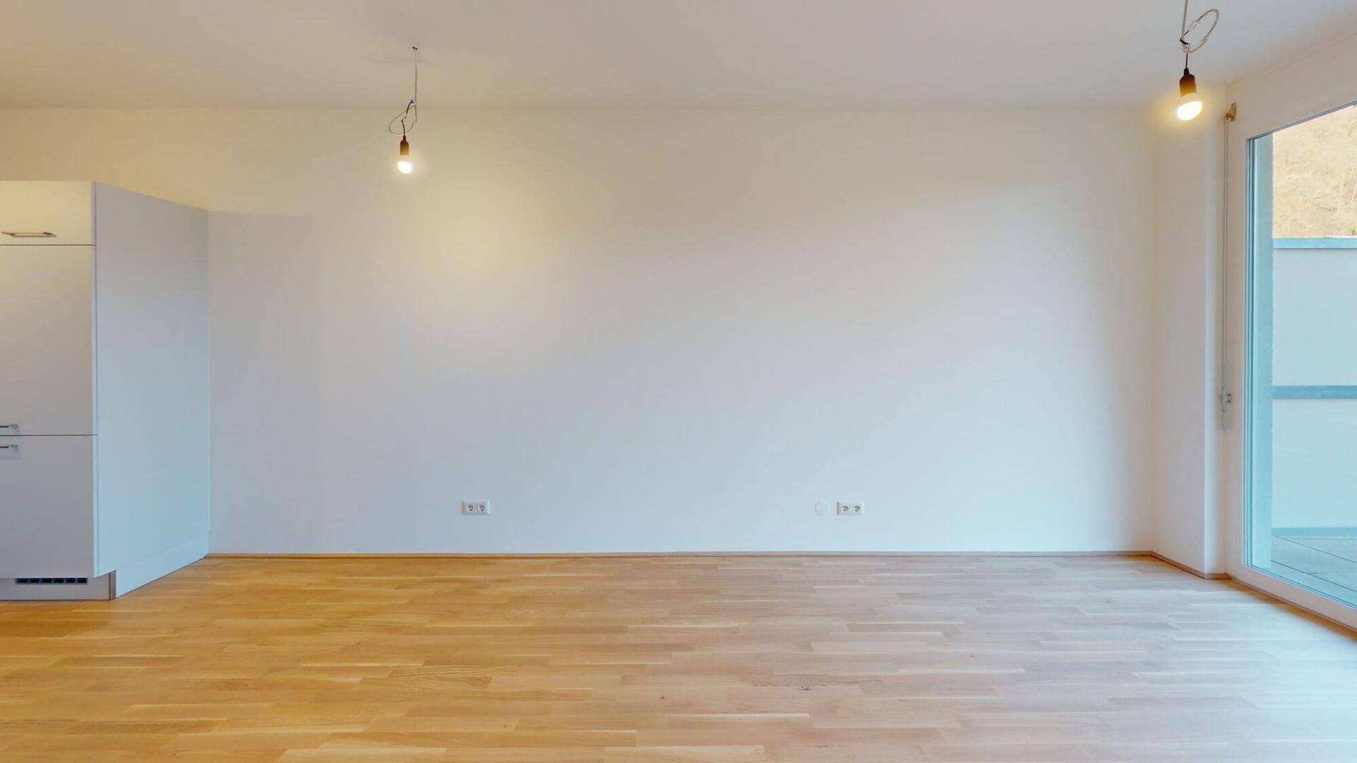 Geräumiger, heller Raum mit Holzboden und Zugang zu einem Außenbereich.