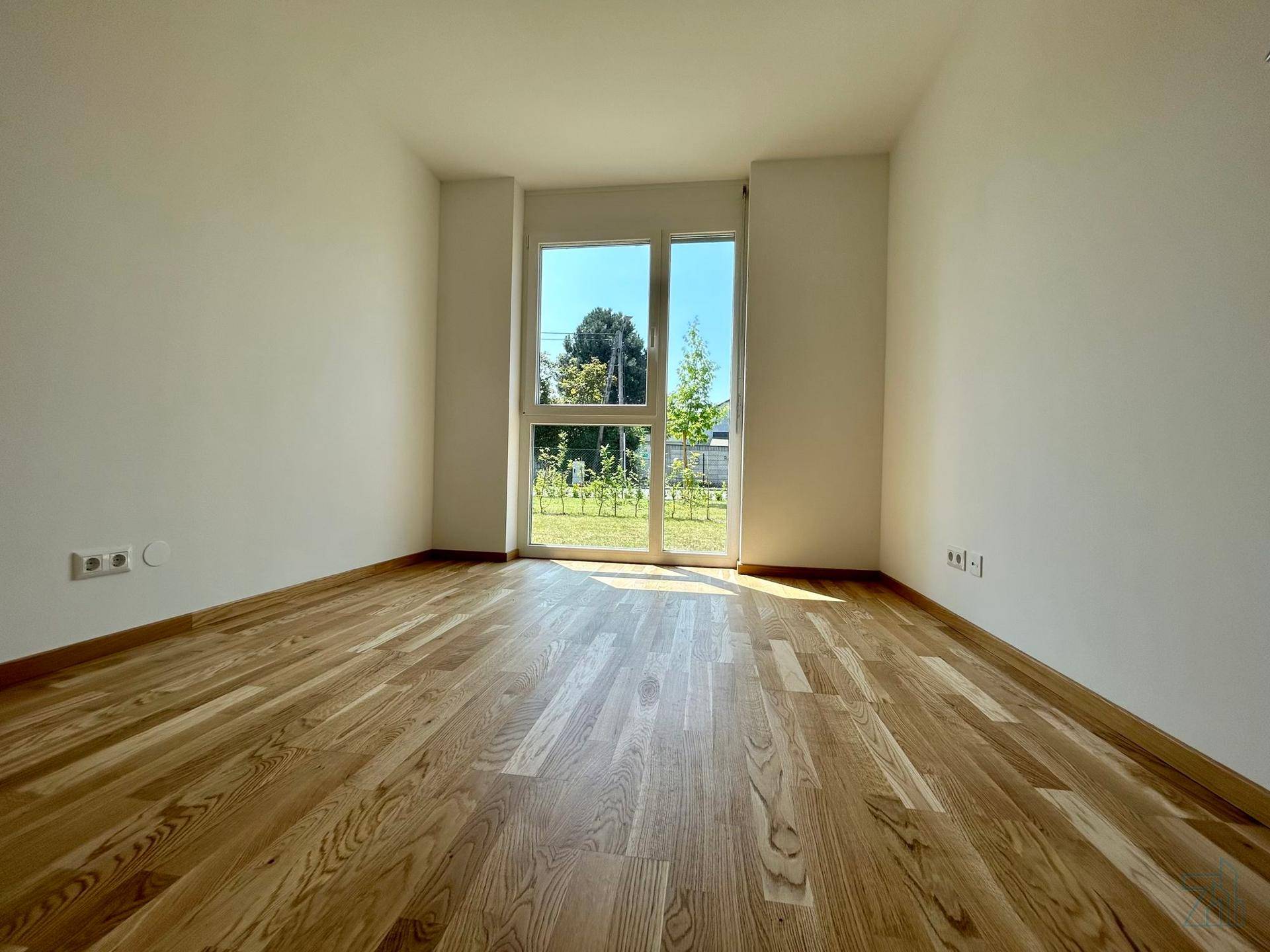 Helles Schlafzimmer mit Holzboden und großen Fenstern, die viel Licht hereinlassen.