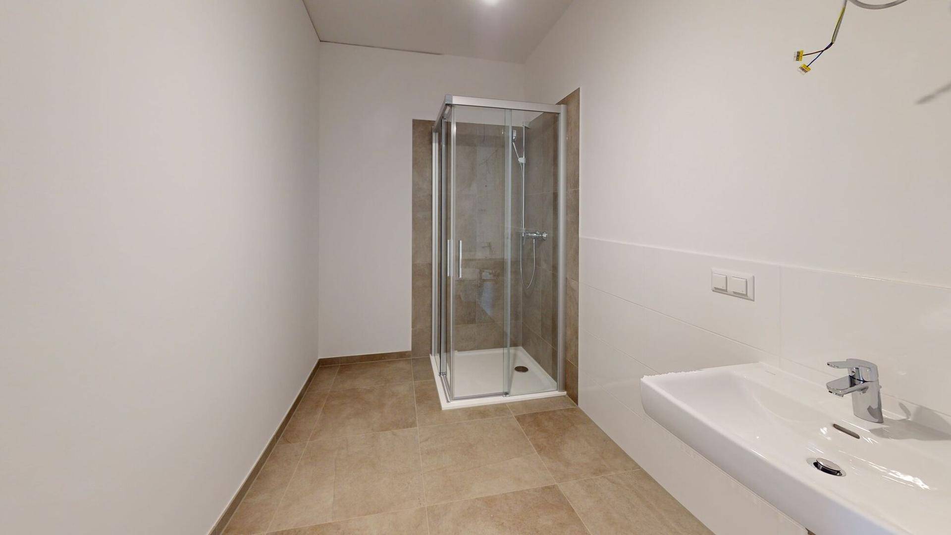 Modernes Badezimmer mit Duschkabine, Waschbecken und hellen, pflegeleichten Fliesen.