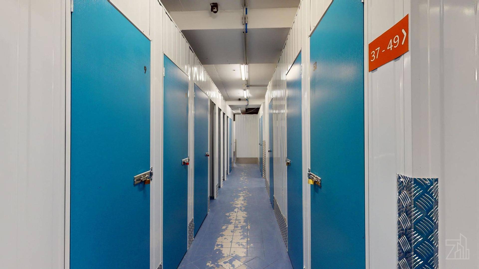 Gang in einem Lagerbereich mit nummerierten blauen Türen und weiß gestreiften Wänden.