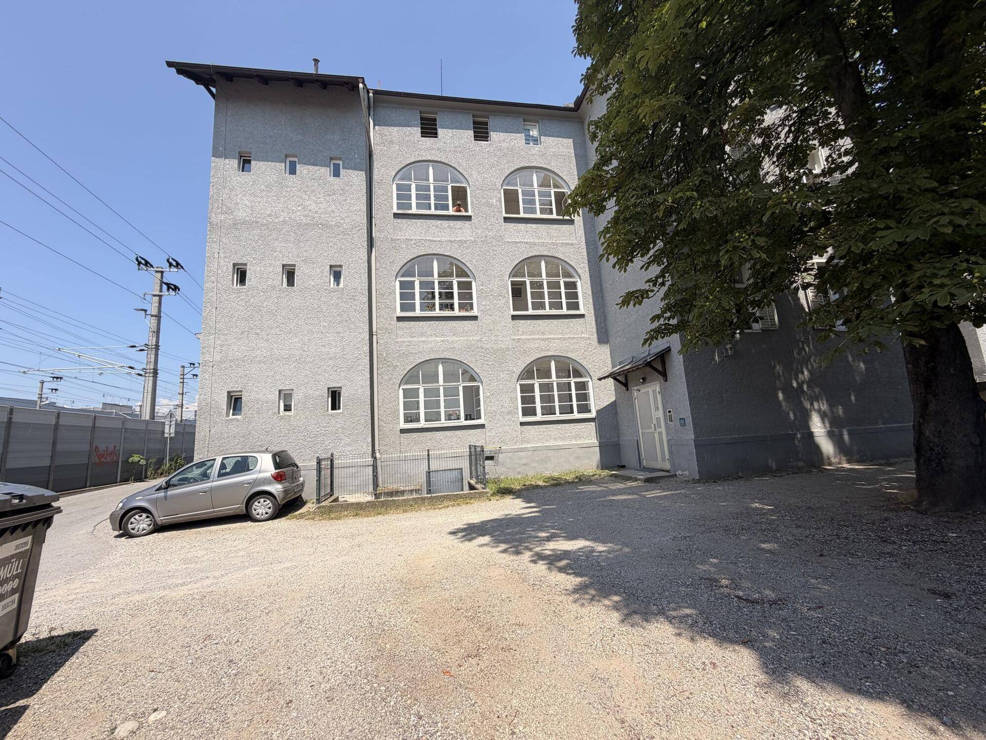 Gesamtansicht des grauen Mehrfamilienhauses mit vielen Fenstern und Parkplätzen.