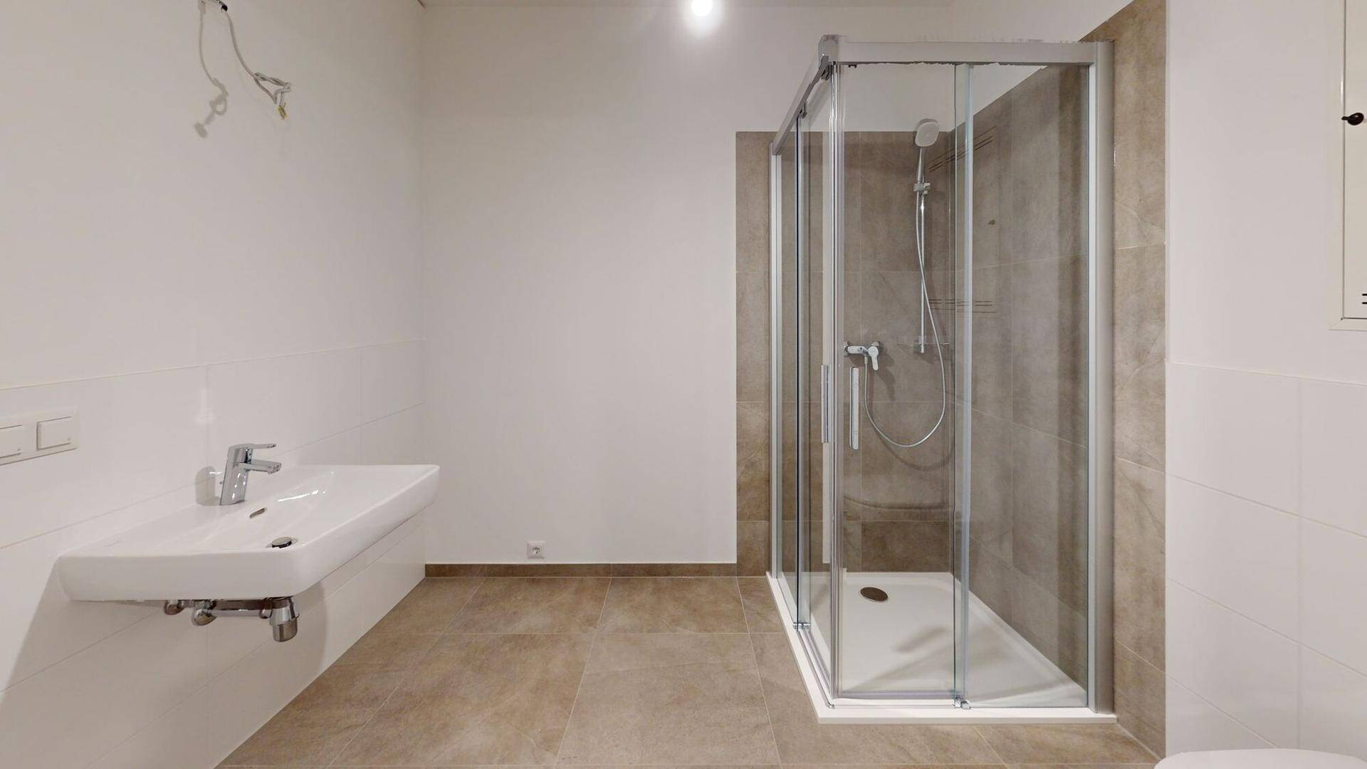 Modernes Badezimmer mit Duschkabine, Waschbecken und hellen Fliesen an Boden und Wänden.