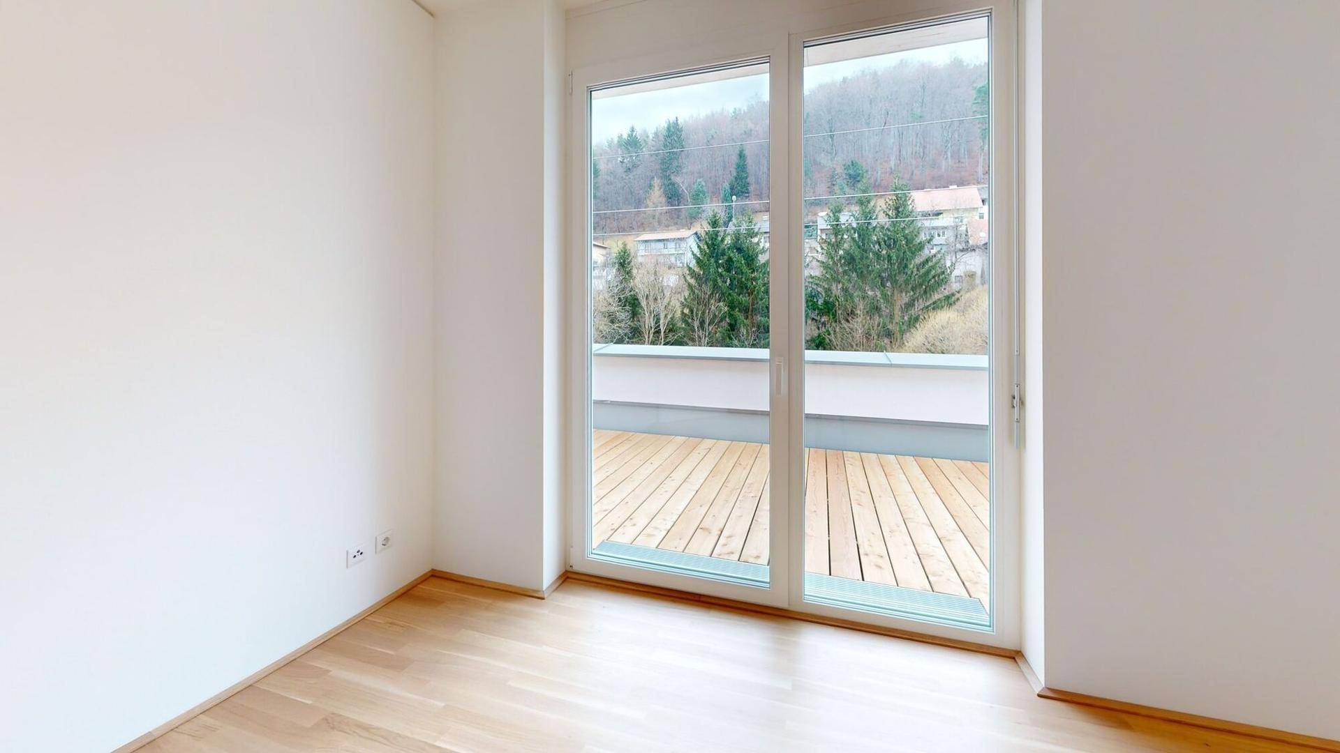 Heller Raum mit Holzboden und großen Fenstern, die einen Blick auf die umliegende Natur bieten.